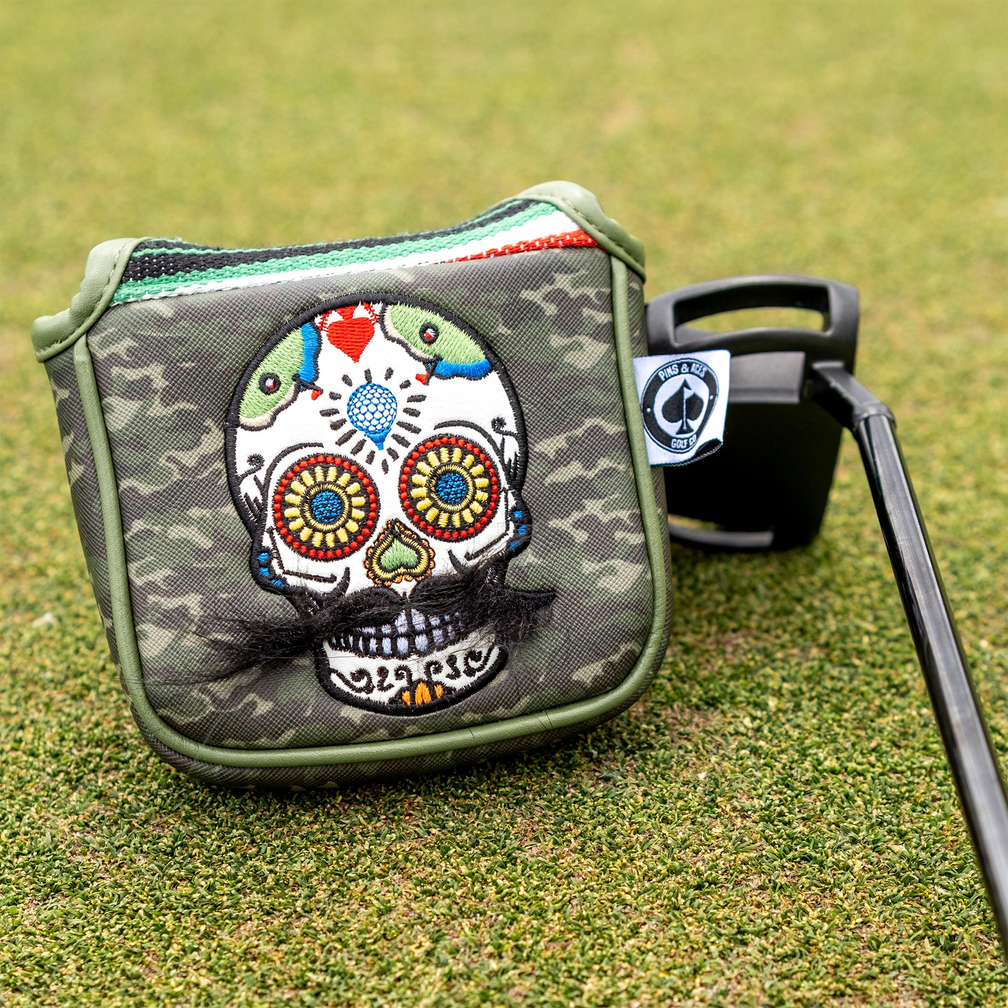 Colorful embroidered skull headcover with mustache, on green camouflage golf bag with bold design, perfect for standout go...