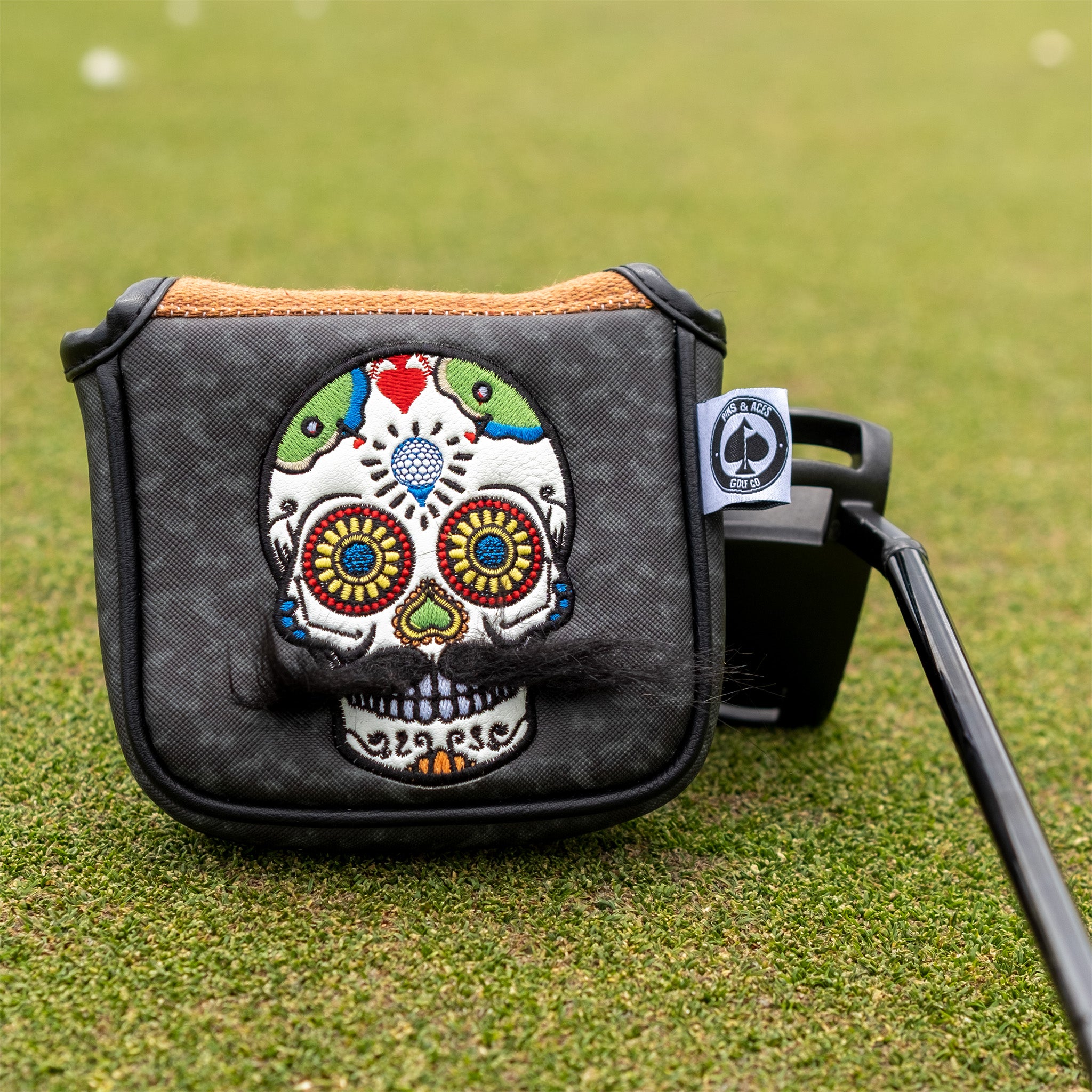 Colorful embroidered skull golf headcover with vibrant designs, attached to a black golf club on the course.