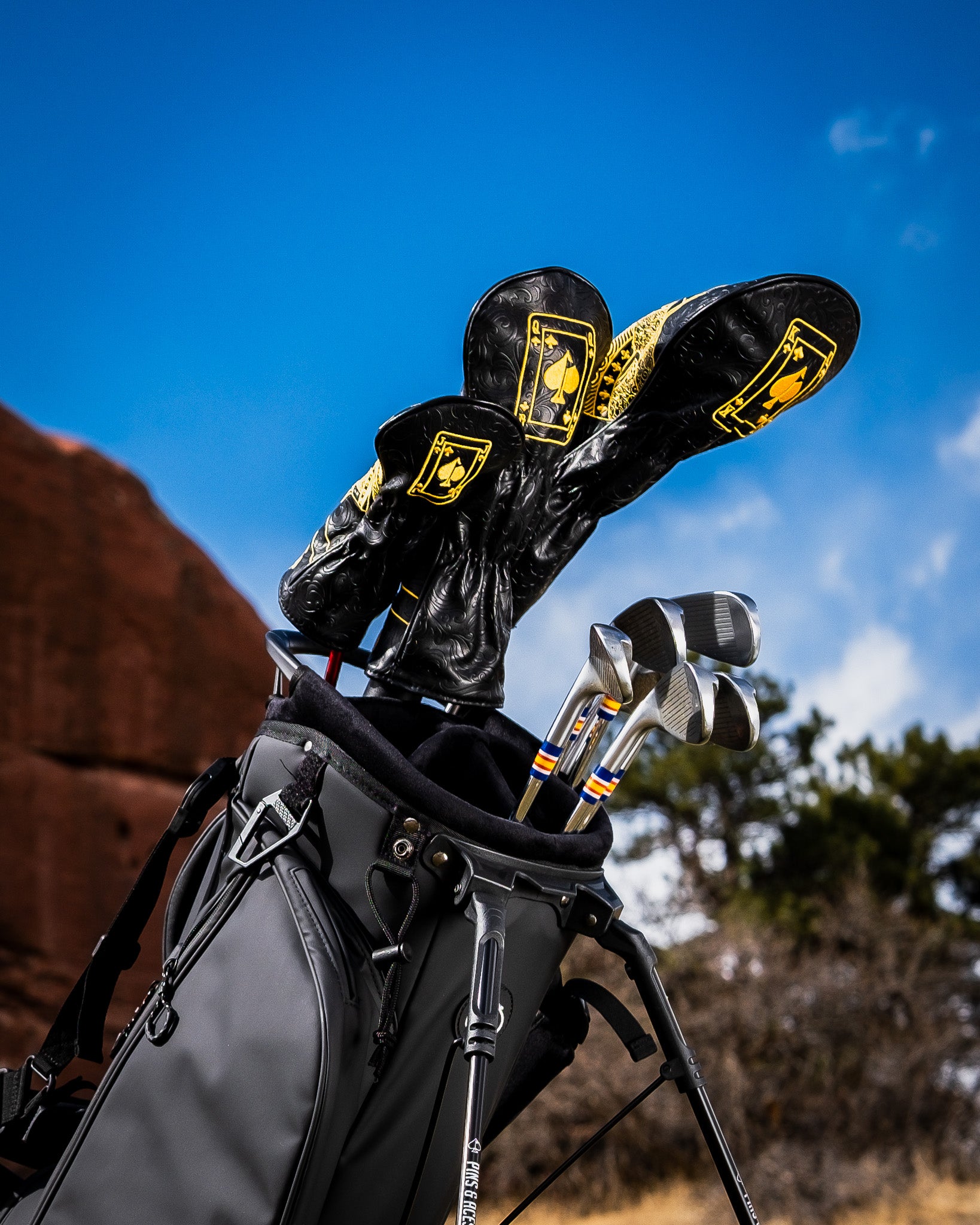 Golf bag with black and yellow headcovers featuring playing card designs, set against a blue sky.