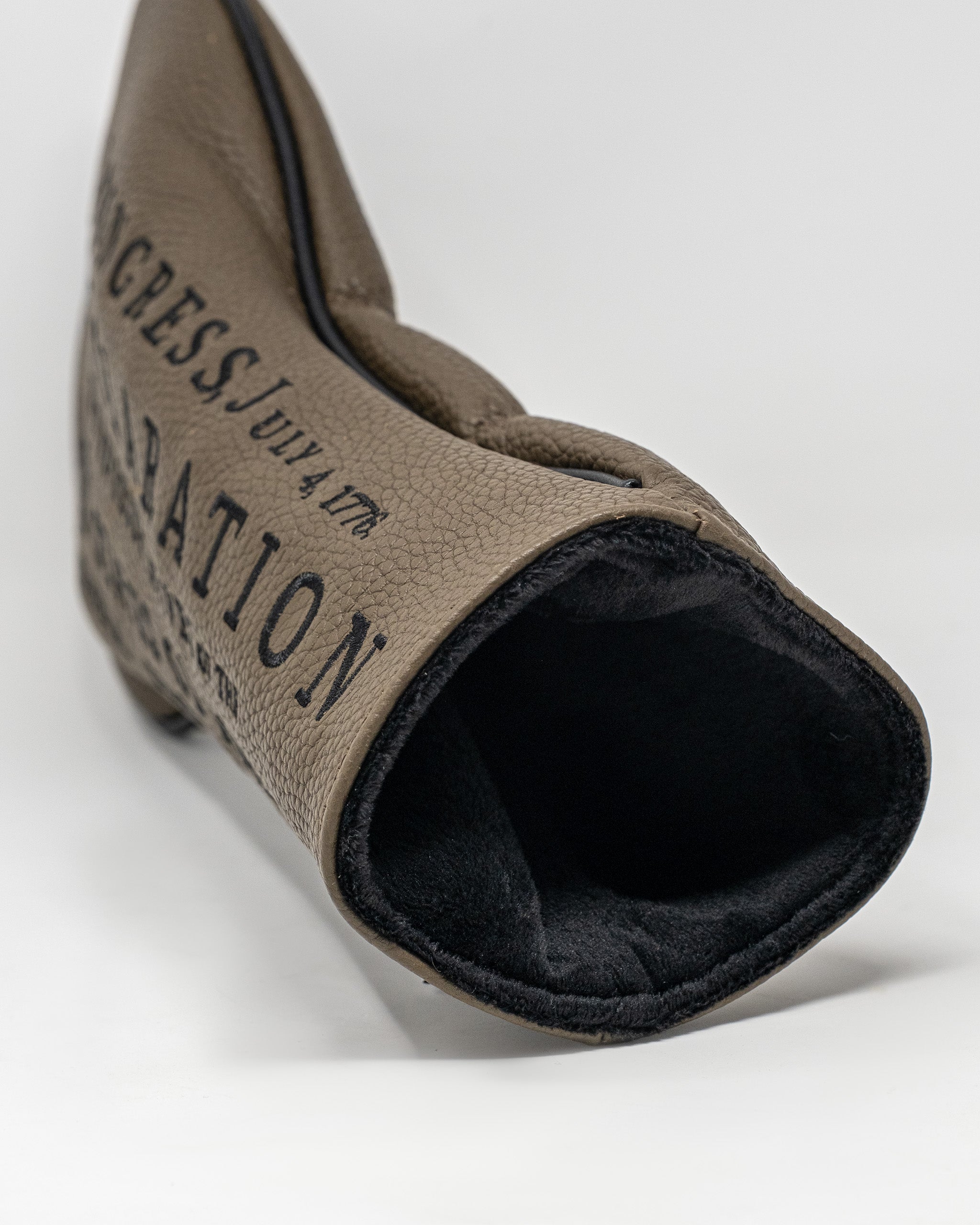 Driver cover with beige and black material, featuring printed text and designed to protect golf club drivers.