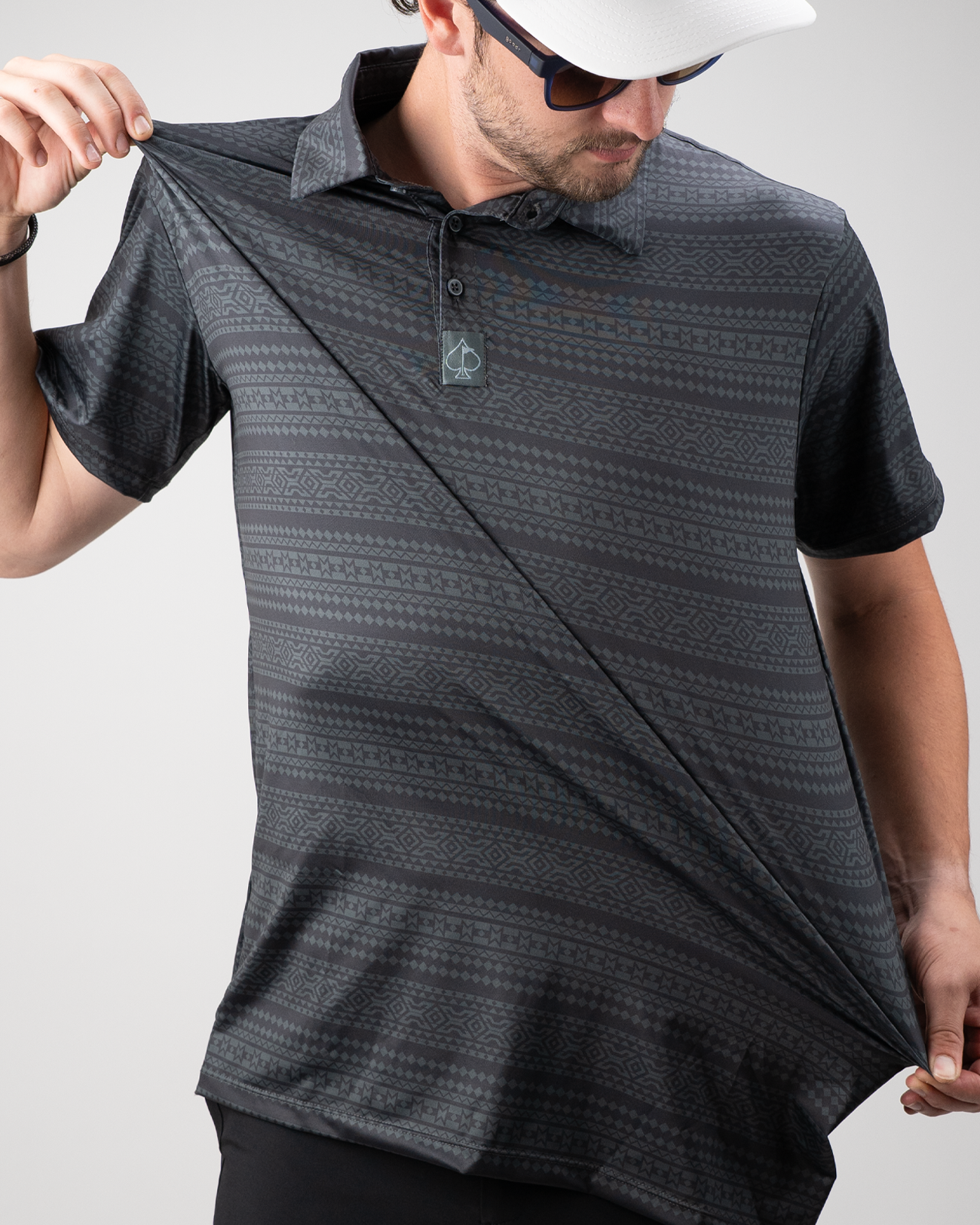 A golfer showcasing the Desert Geo polo shirt, featuring a geometric pattern in shades of black and gray.