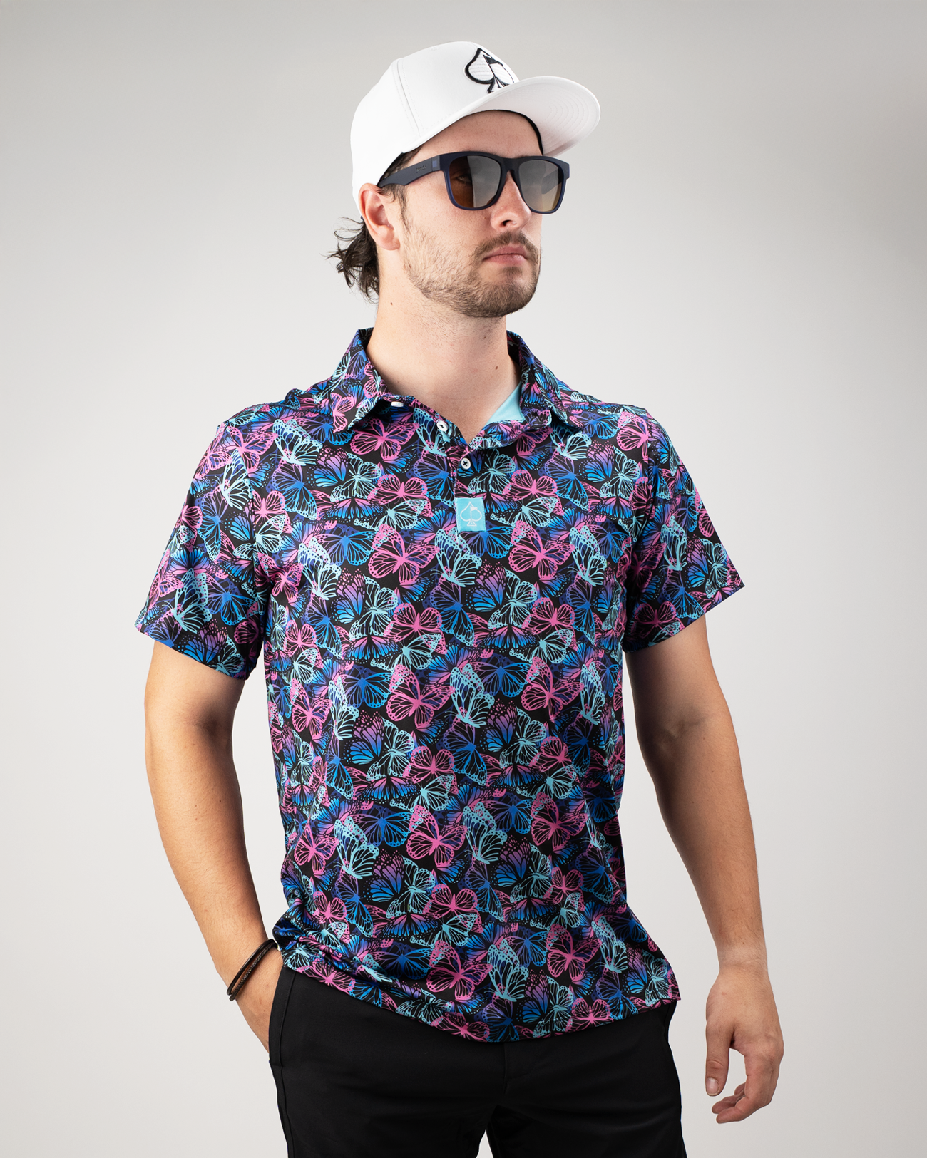 Man wearing a vibrant Electric Butterfly golf polo featuring a colorful butterfly and floral pattern, paired with sunglasses and a cap.