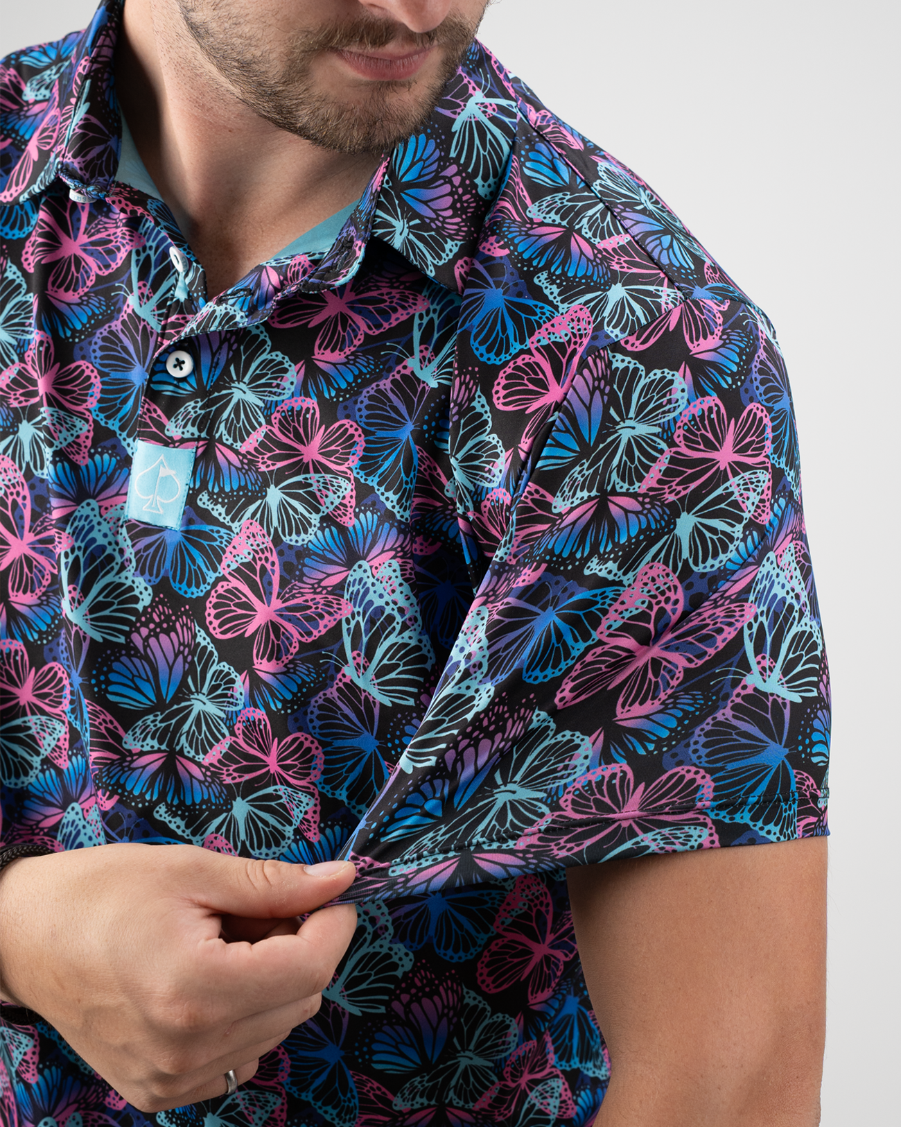 A man showcasing the vibrant Electric Butterfly golf shirt with a colorful butterfly pattern on a black background.