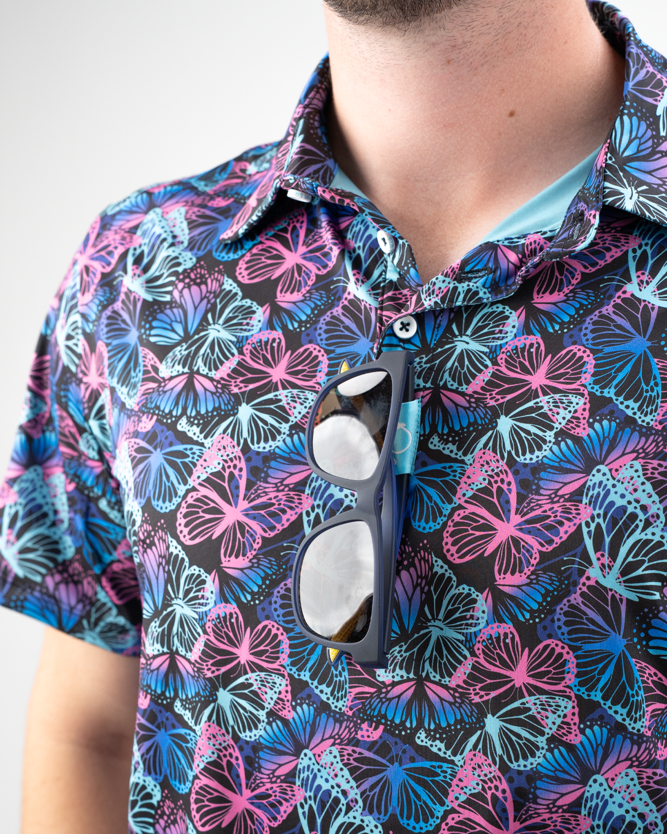 Colorful polo shirt featuring a vibrant butterfly pattern in shades of pink, blue, and purple, worn by a model.