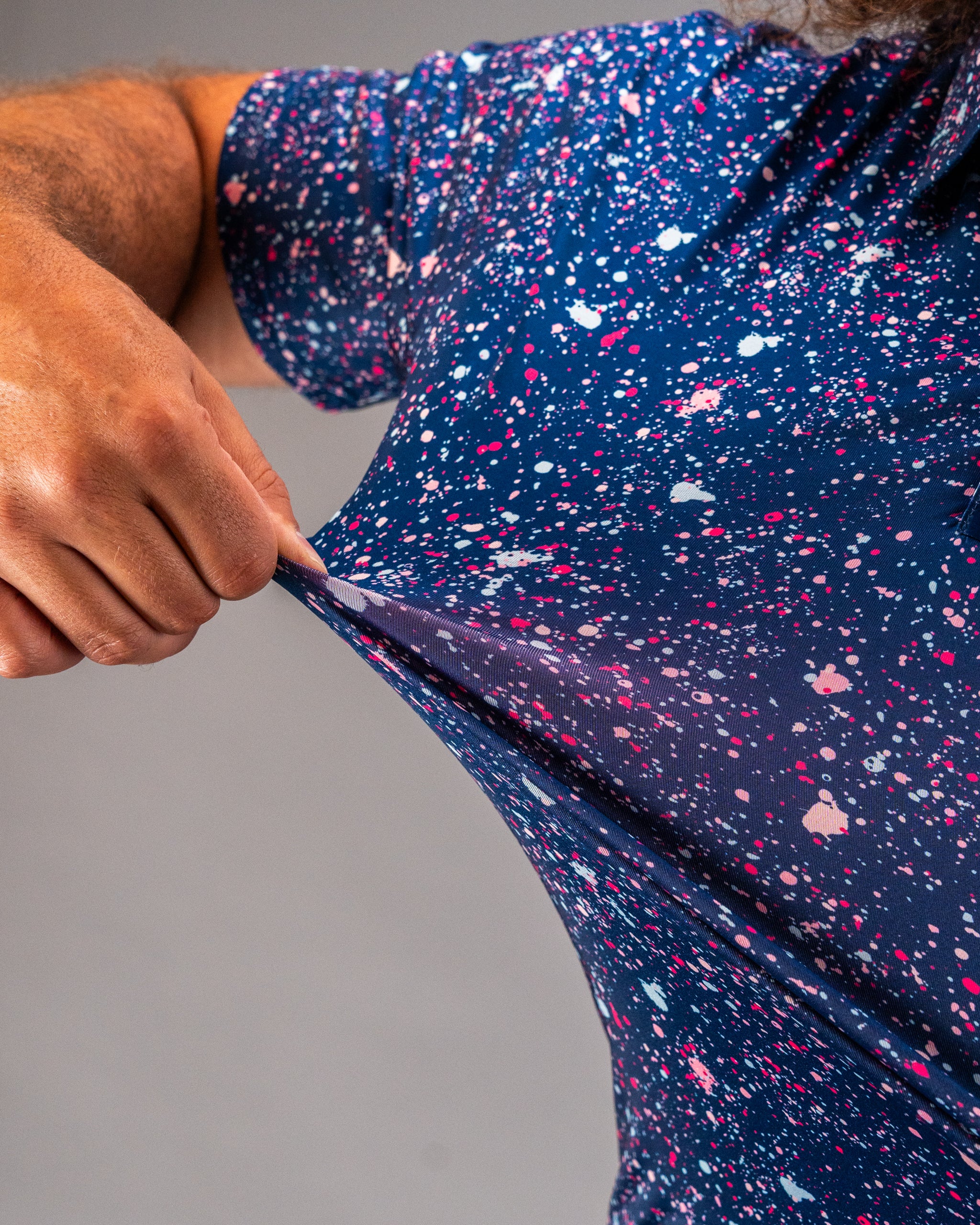 Bold blue splatter golf shirt featuring vibrant splashes of pink and white, showcasing its stretchy fabric and unique design.