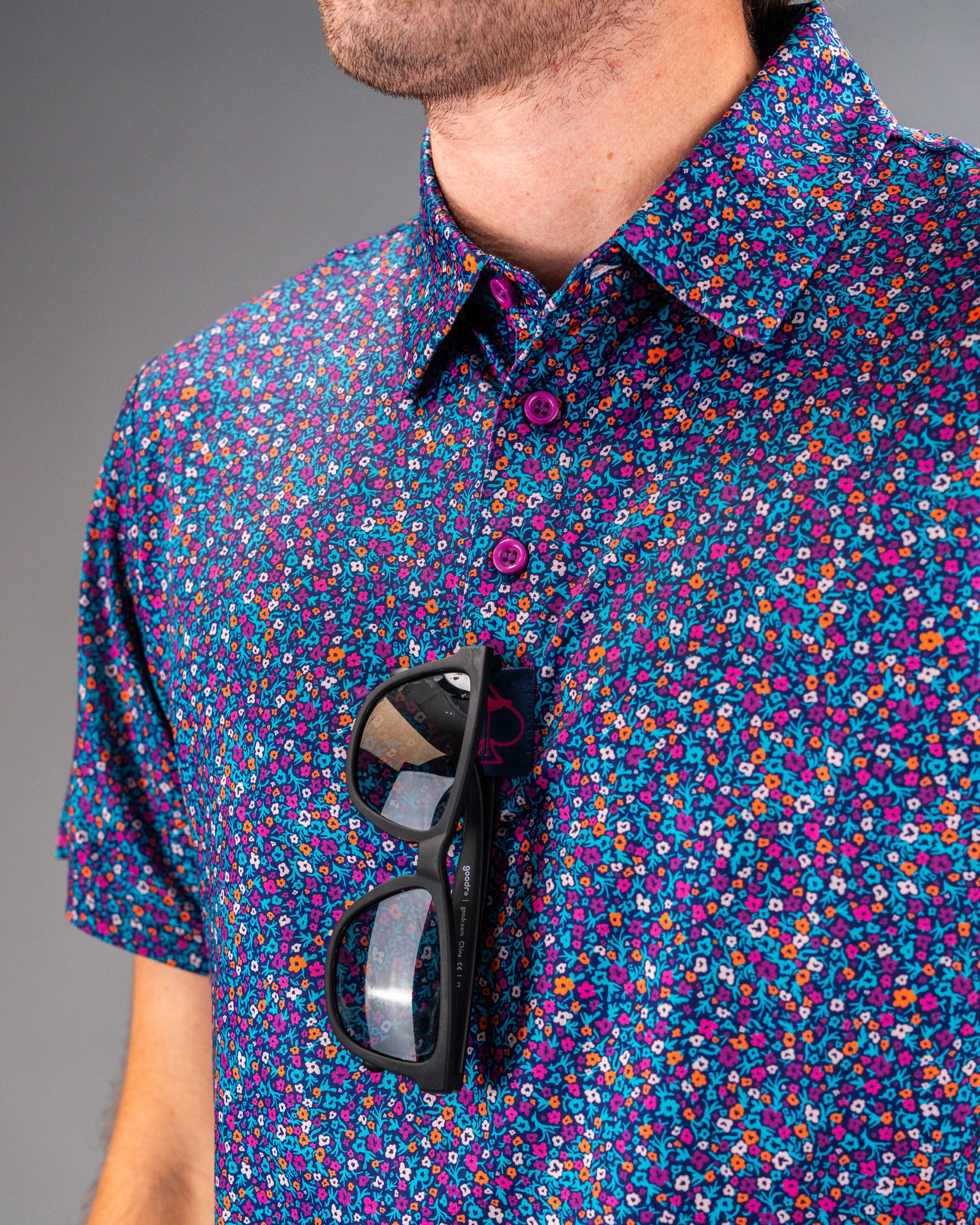 Bold golf shirt featuring a vibrant lavender floral pattern, complemented by stylish sunglasses hanging from the collar.