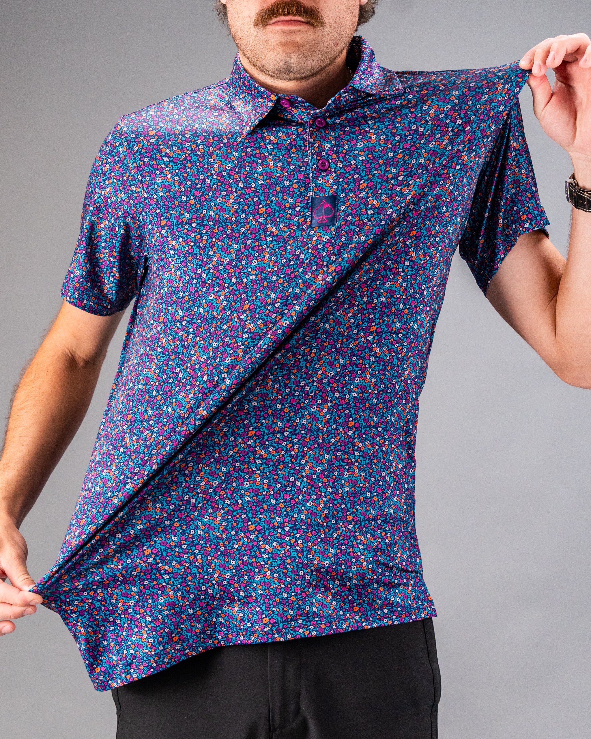 Lavender Flower Power golf shirt featuring a vibrant floral pattern, showcased by a model pulling the fabric.