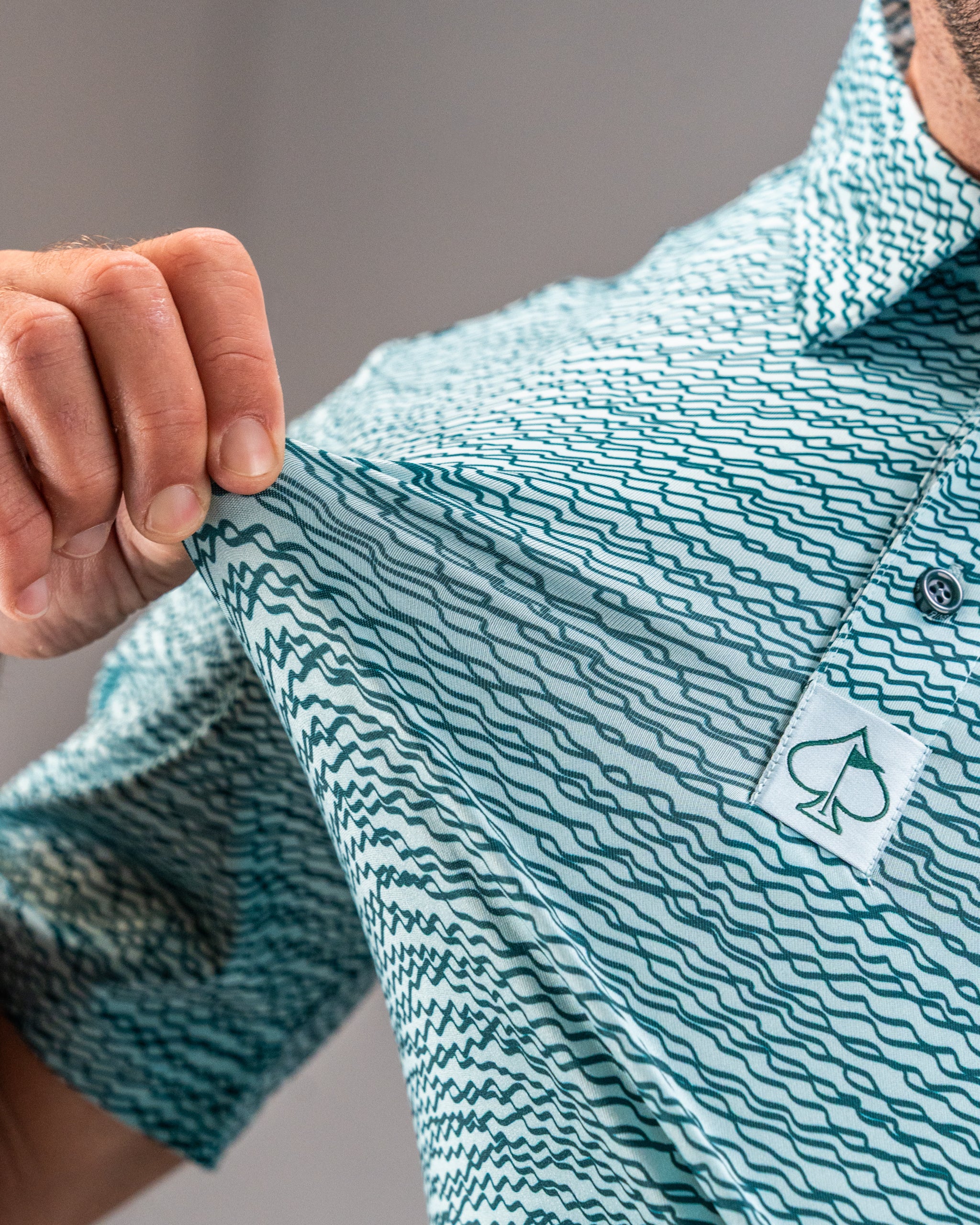 Teal golf polo featuring a squiggle pattern and a logo on the collar, showcasing its lightweight and breathable fabric.