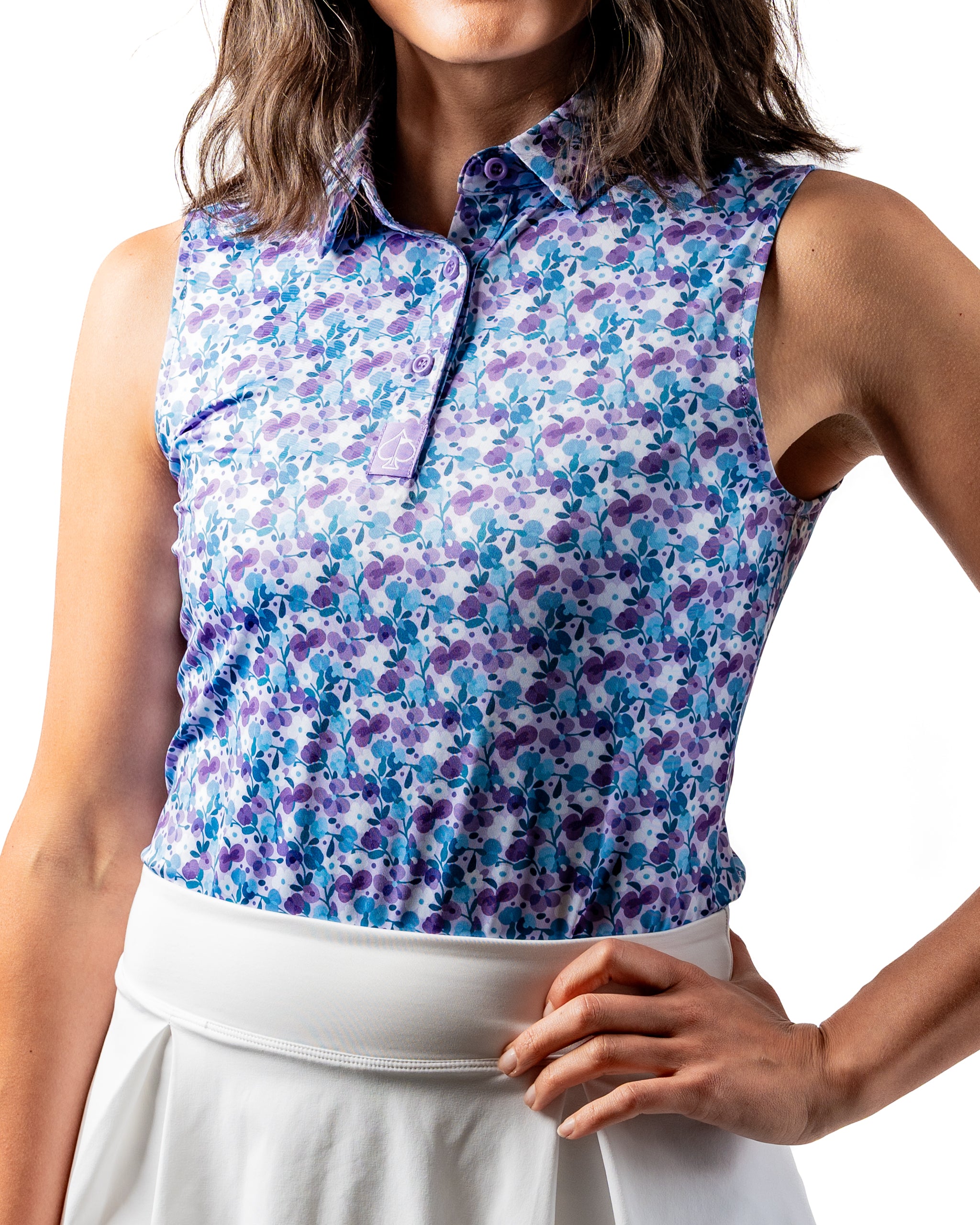 Women's sleeveless white golf top featuring a vibrant floral pattern in shades of purple and blue, perfect for stylish play.
