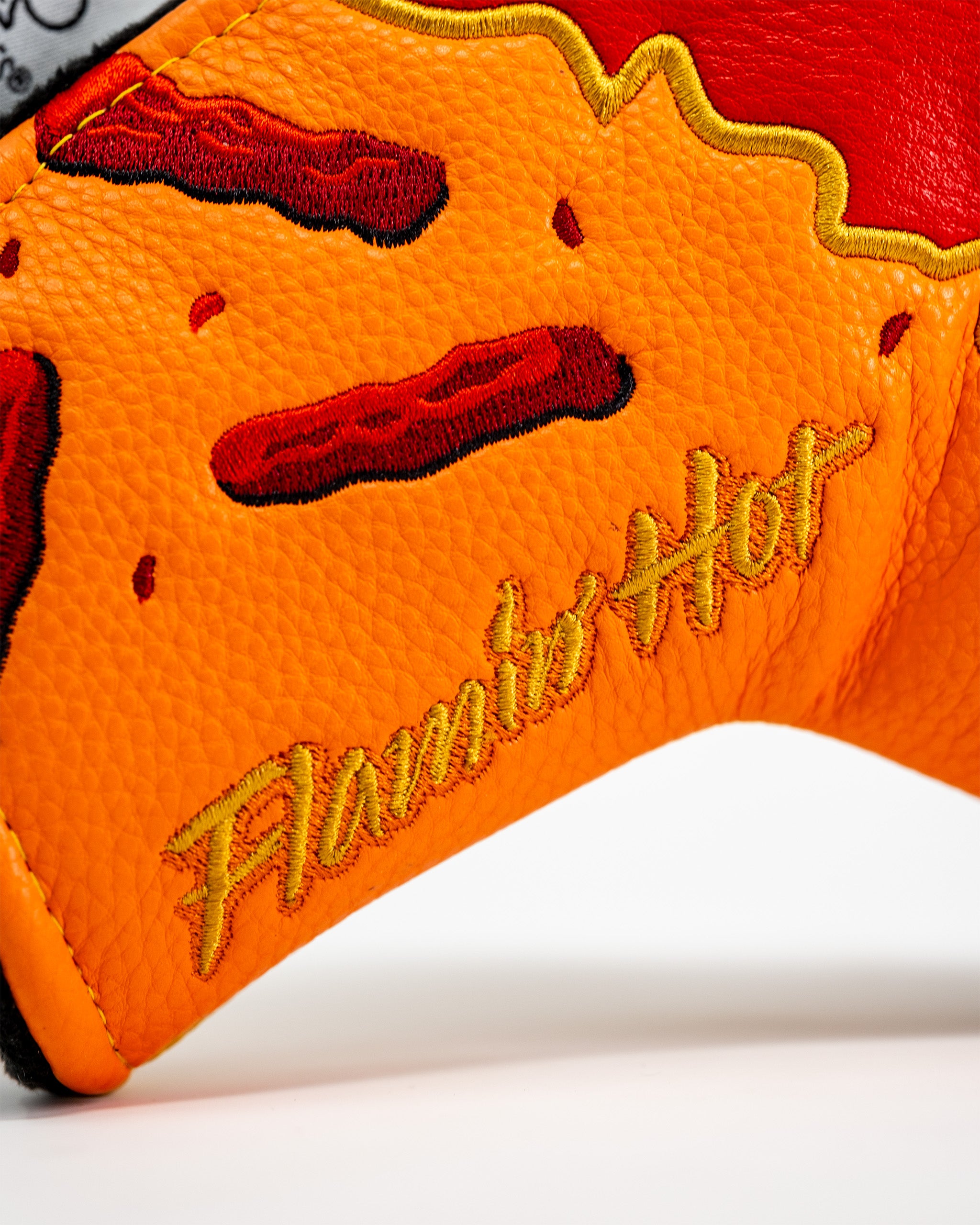 Close-up of an embroidered blade putter cover featuring a hot dog design, orange textured material, and "Flamin' Hot" text.