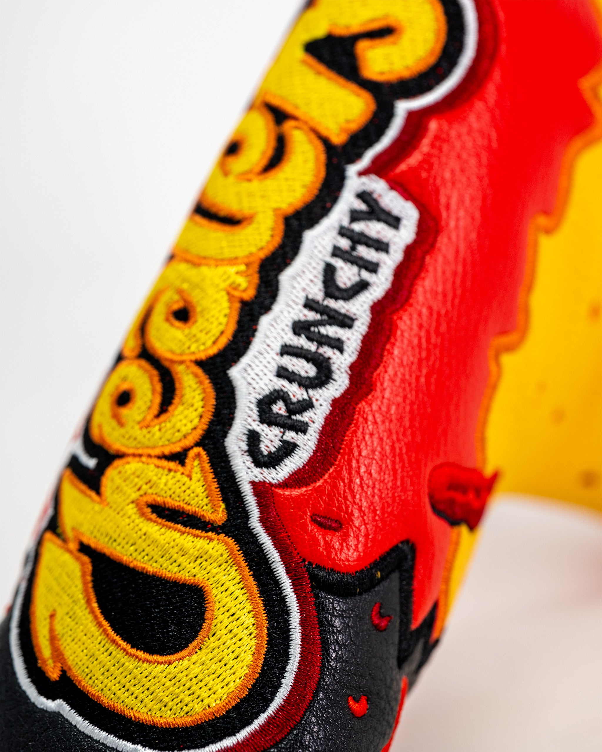 Close-up of a vibrant embroidered blade putter cover featuring the Flamin' Hot Cheaters logo with red, yellow, black, and white details.