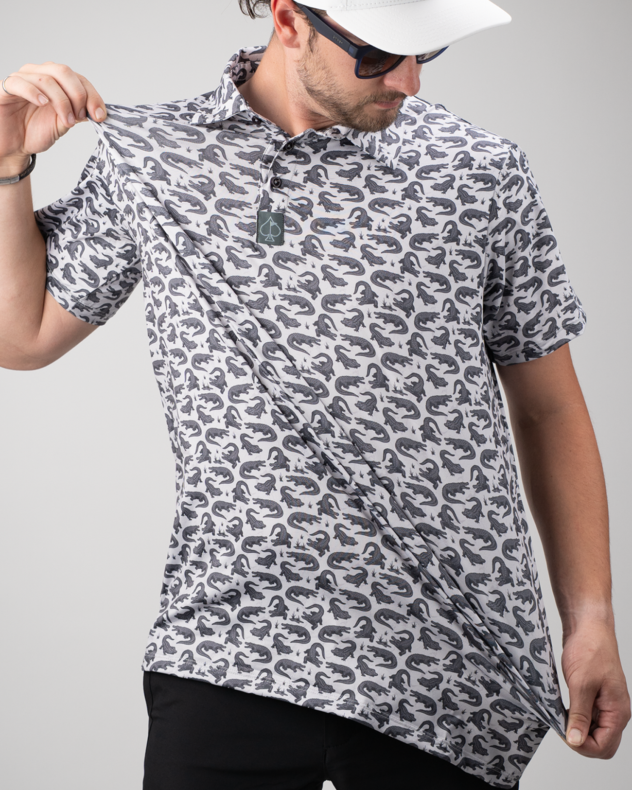 Men's golf polo shirt featuring a bold gator print in gray and black, worn by a man adjusting the fabric.