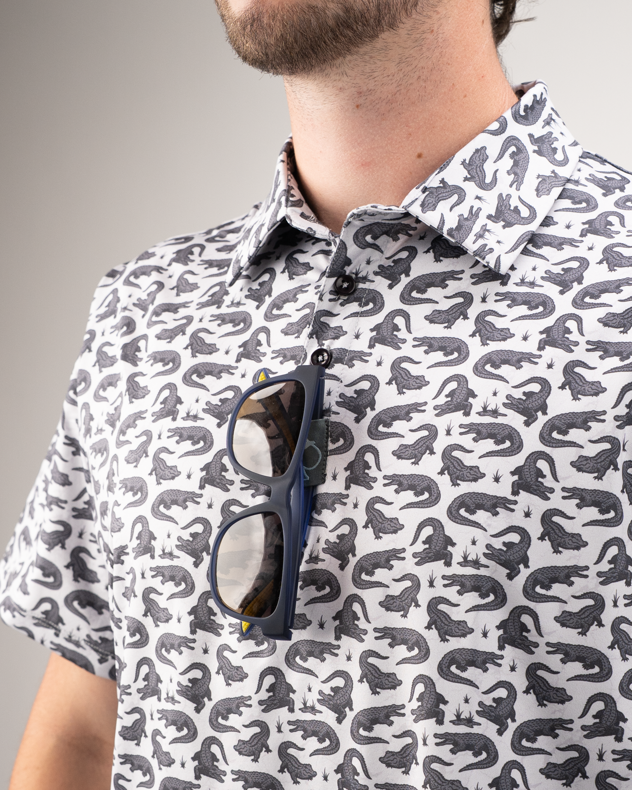 Men's golf shirt featuring a playful alligator print, paired with stylish sunglasses for a bold on-course look.