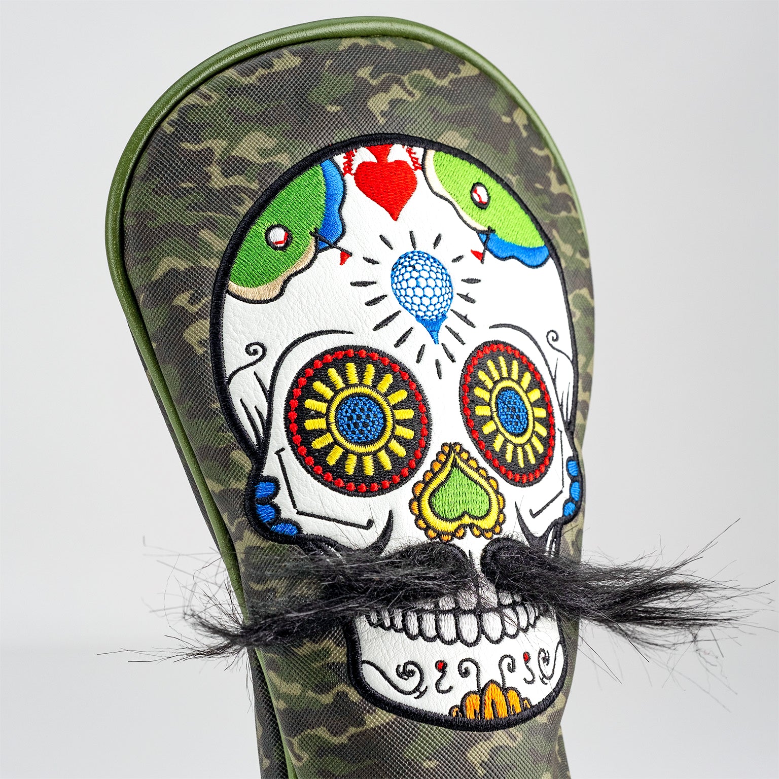 Colorful embroidered sugar skull golf headcover with faux mustache, on camouflage-patterned cover for bold style.