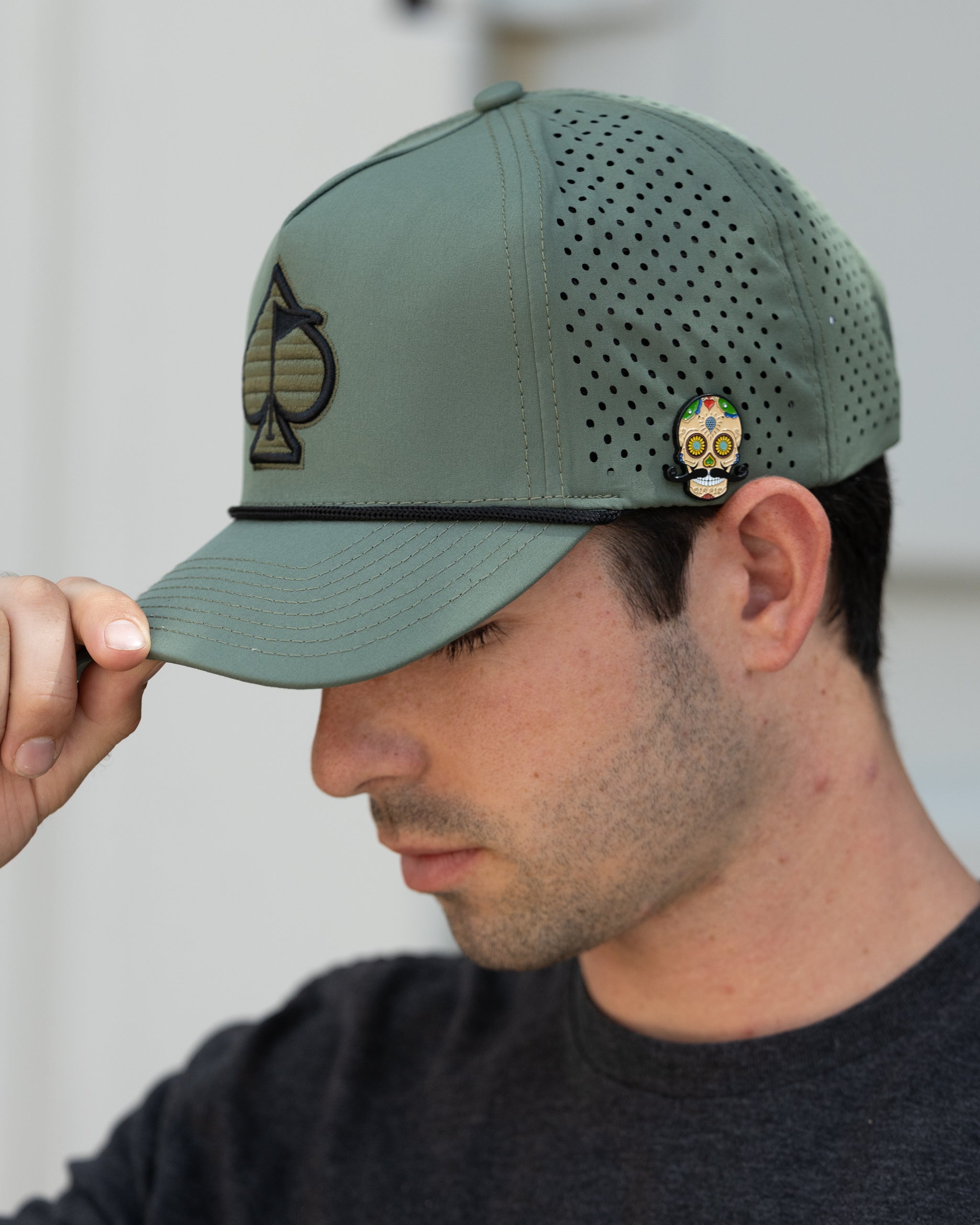 Perforated olive rope hat displayed outdoors, featuring a wide brim and adjustable chin strap.