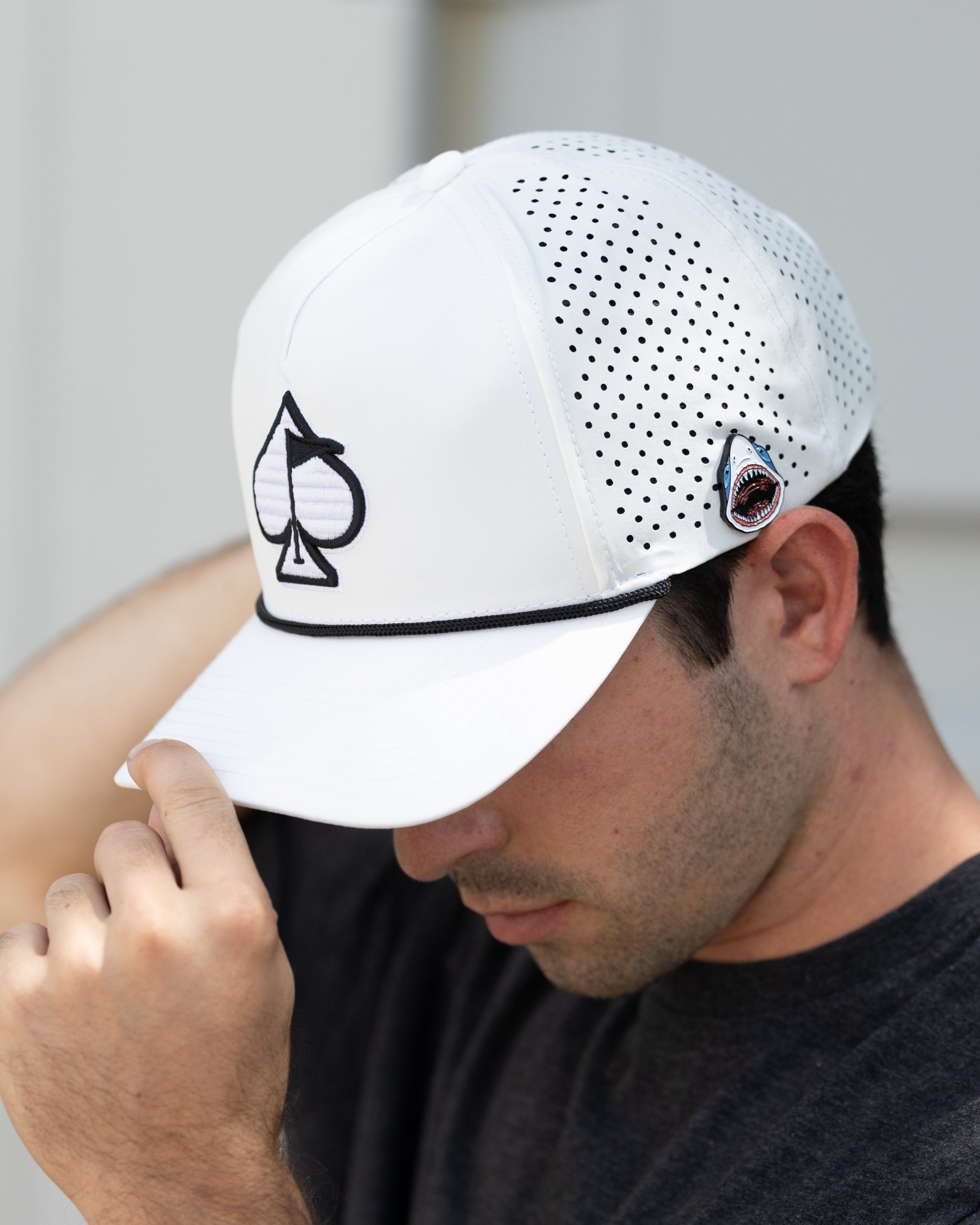 White golf cap with perforated panels, spade logo embroidery, and shark patch, designed for bold, standout golf style.
