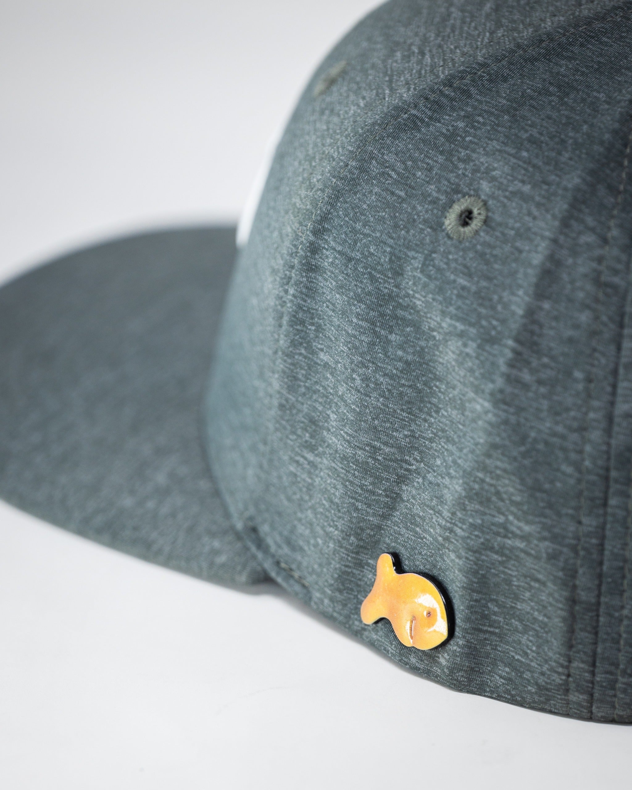 Ash-colored Performance Spade Hat featuring a unique goldfish pin on the side, ideal for stylish golfers.