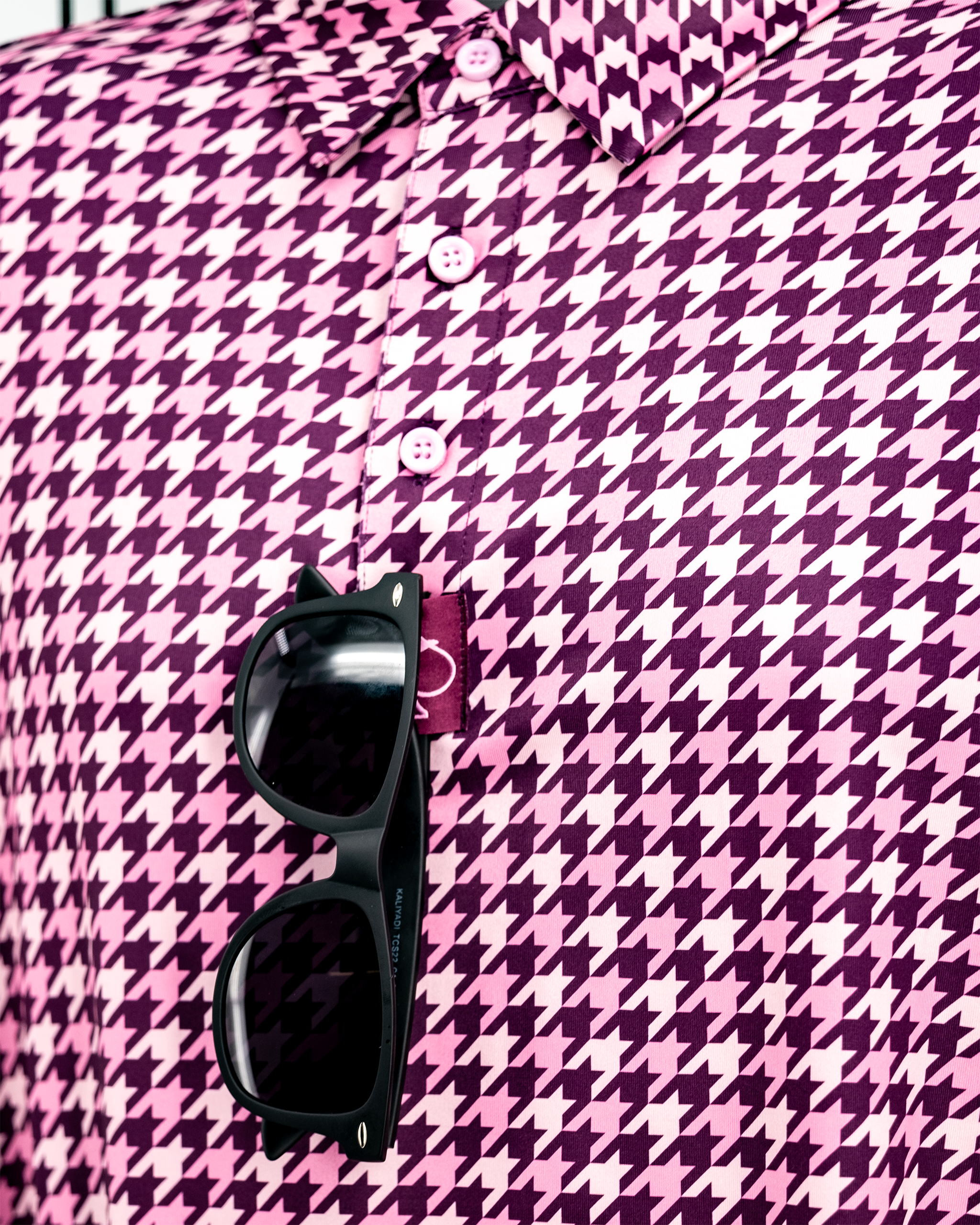 Houndstooth pattern polo in raspberry color displayed on a hanger.