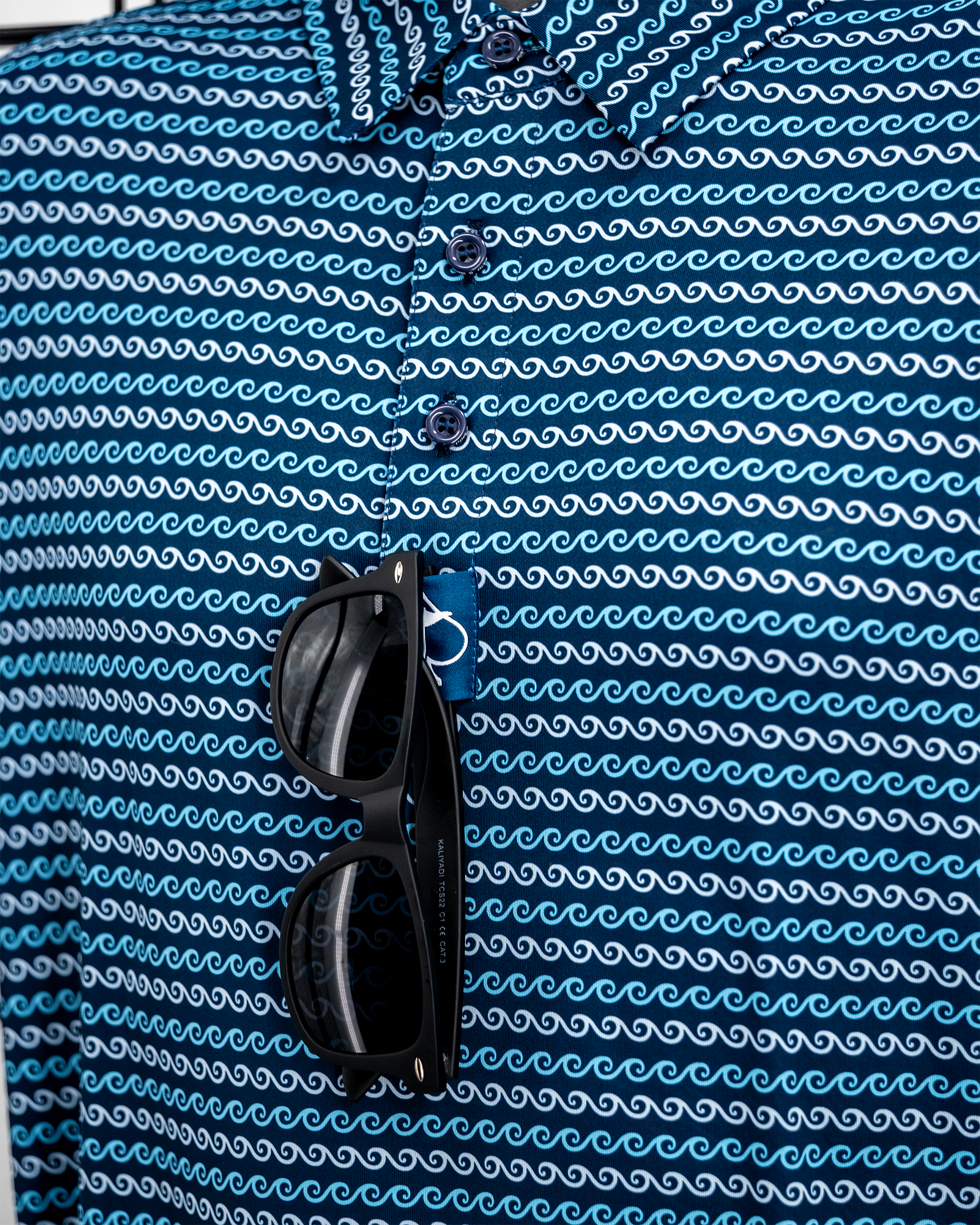 Blue patterned golf shirt with white waves, black sunglasses, and a blue golf towel with white logo.