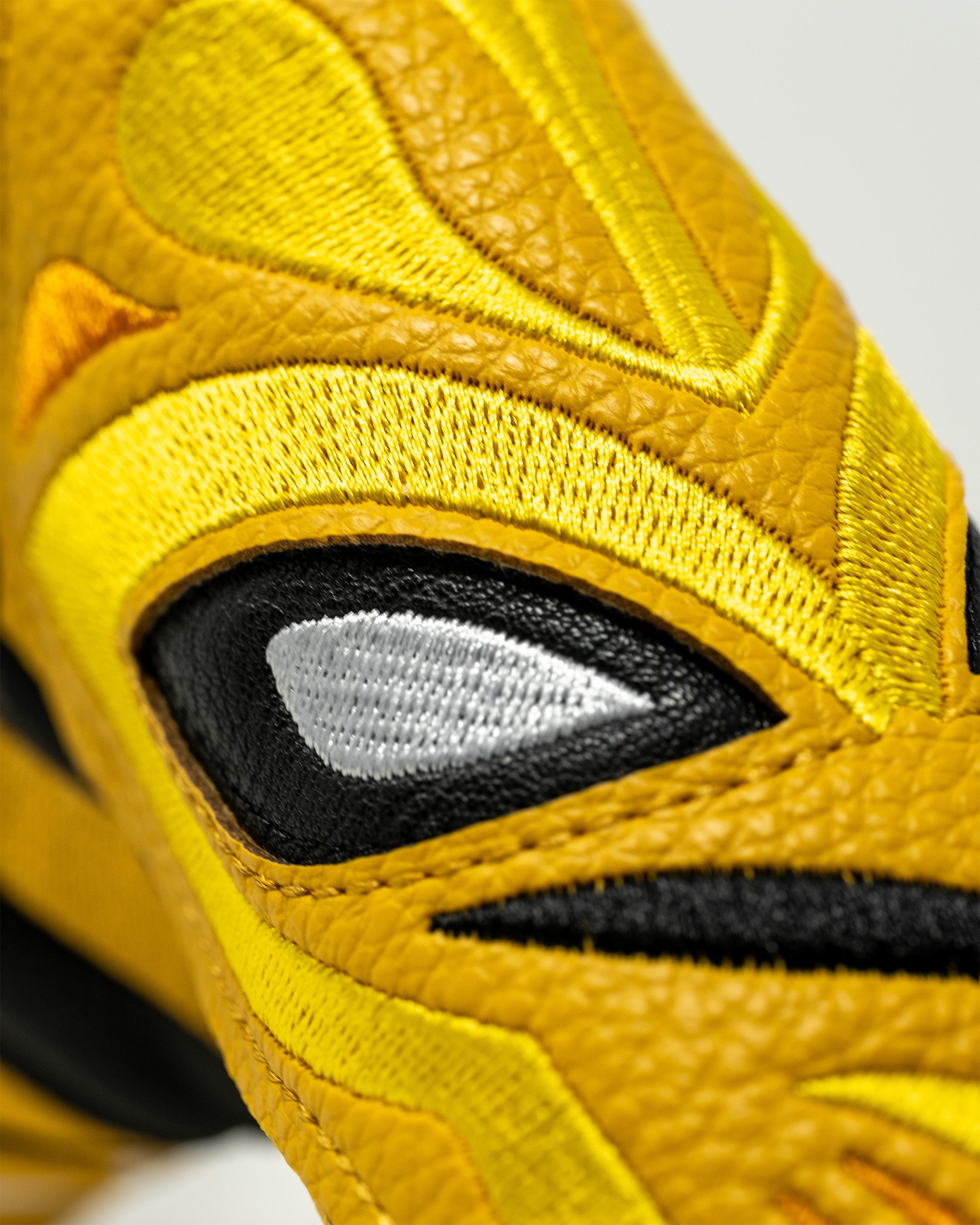 Close-up of a yellow lucha libre mask-themed blade putter cover with embroidered eye details and textured fabric.