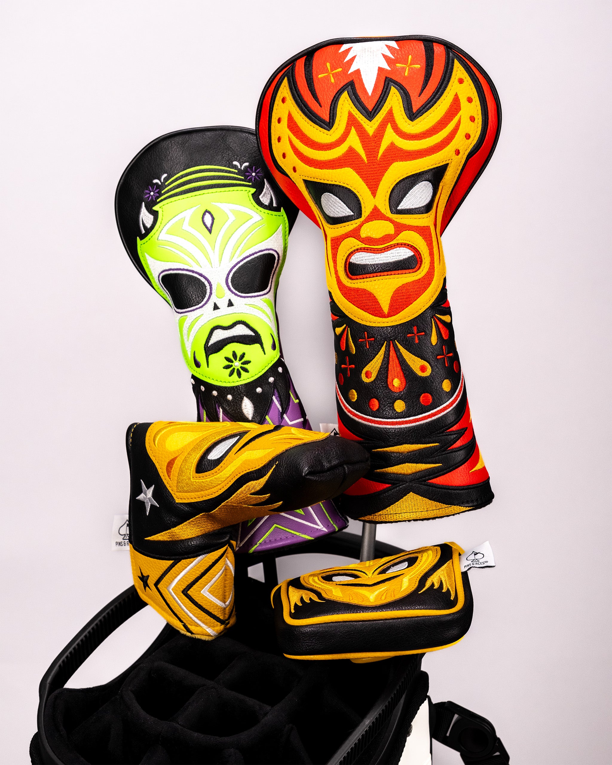 Colorful lucha libre mask-themed mallet putter covers with vibrant Mexican wrestling design, displayed on a golf bag.