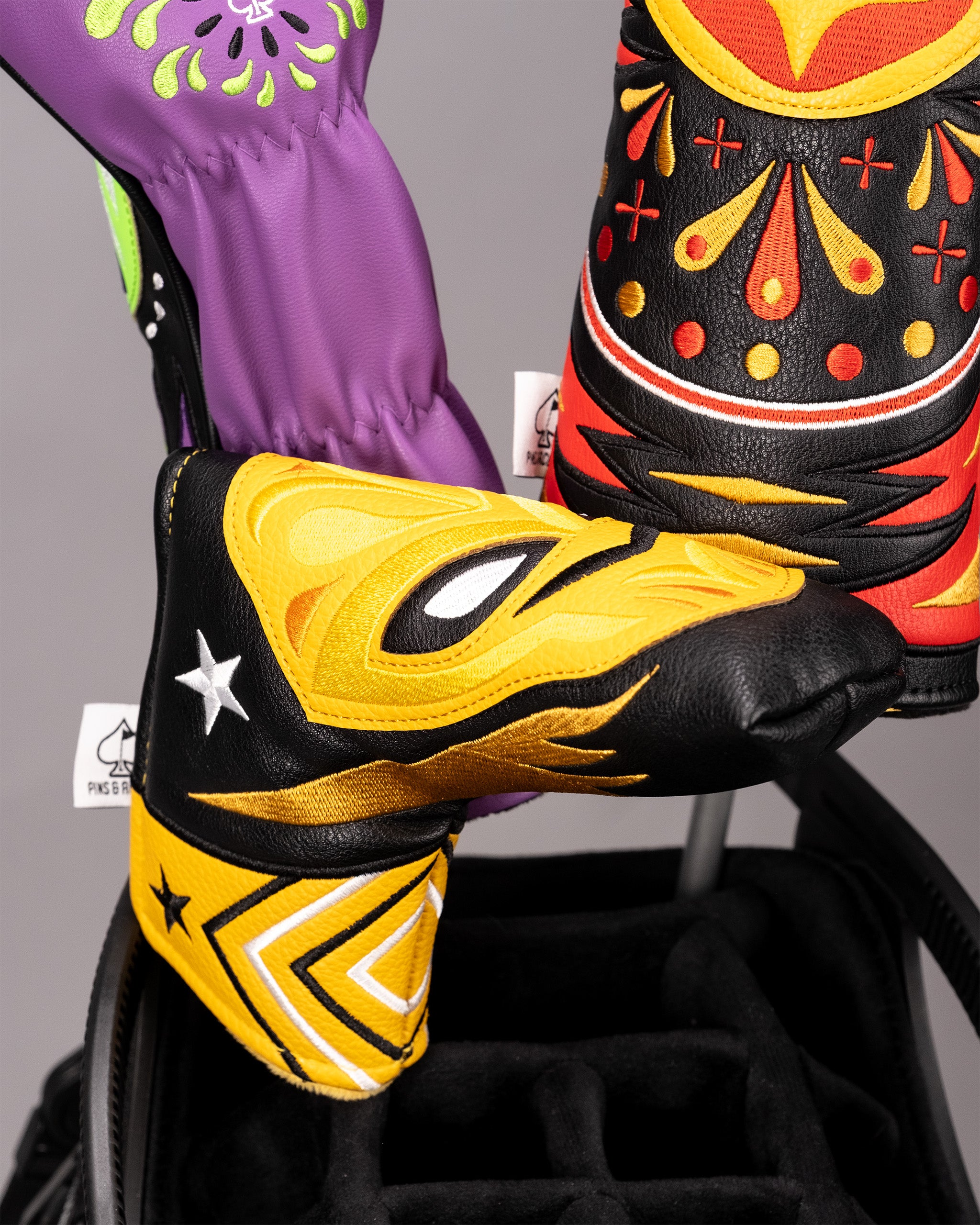 Colorful, bold golf headcovers featuring vibrant yellow, red, black, and purple designs with embroidered patterns and uniq...