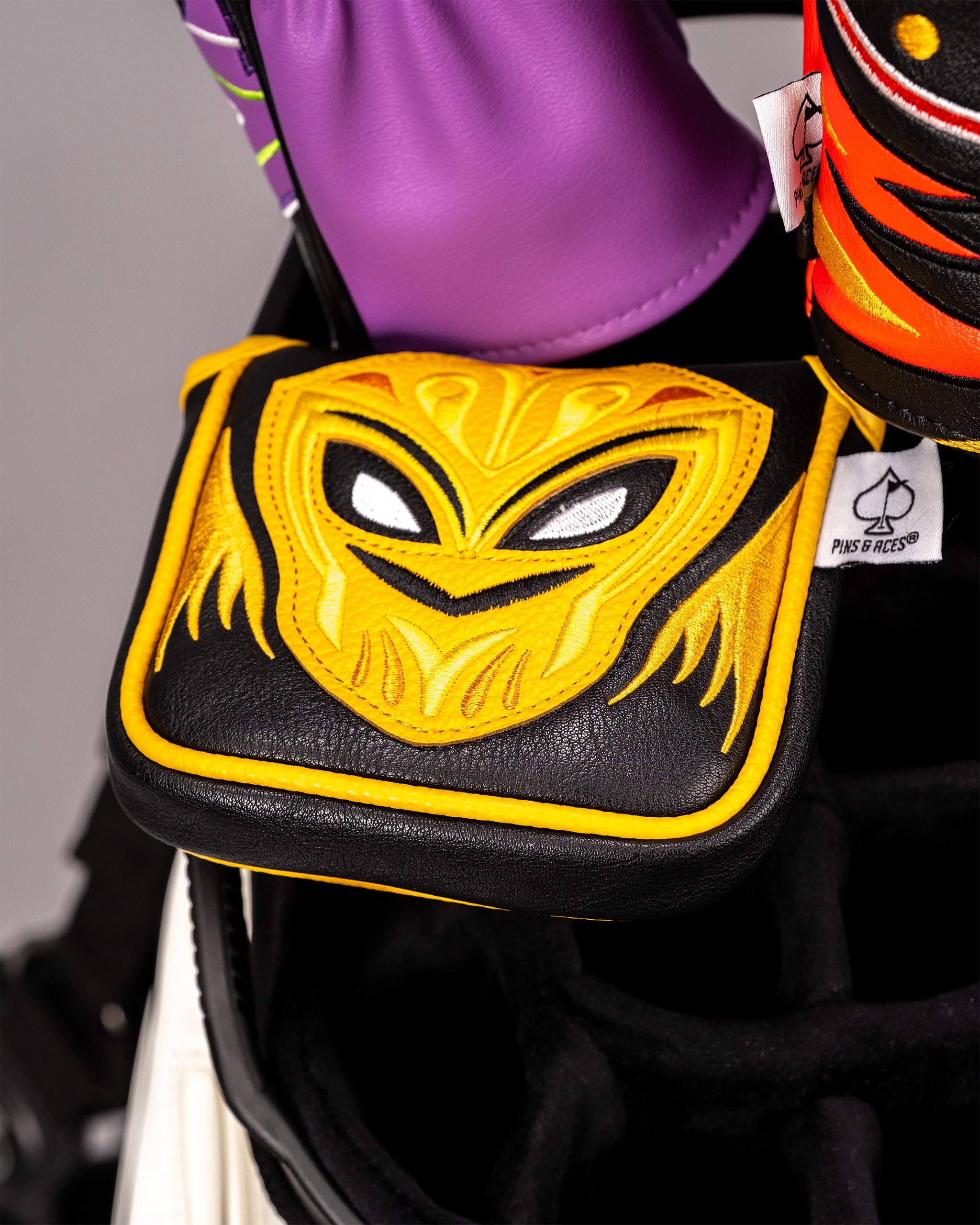 Lucha Libre mask-themed mallet putter cover with a yellow and black embroidered face design, placed on a golf bag.