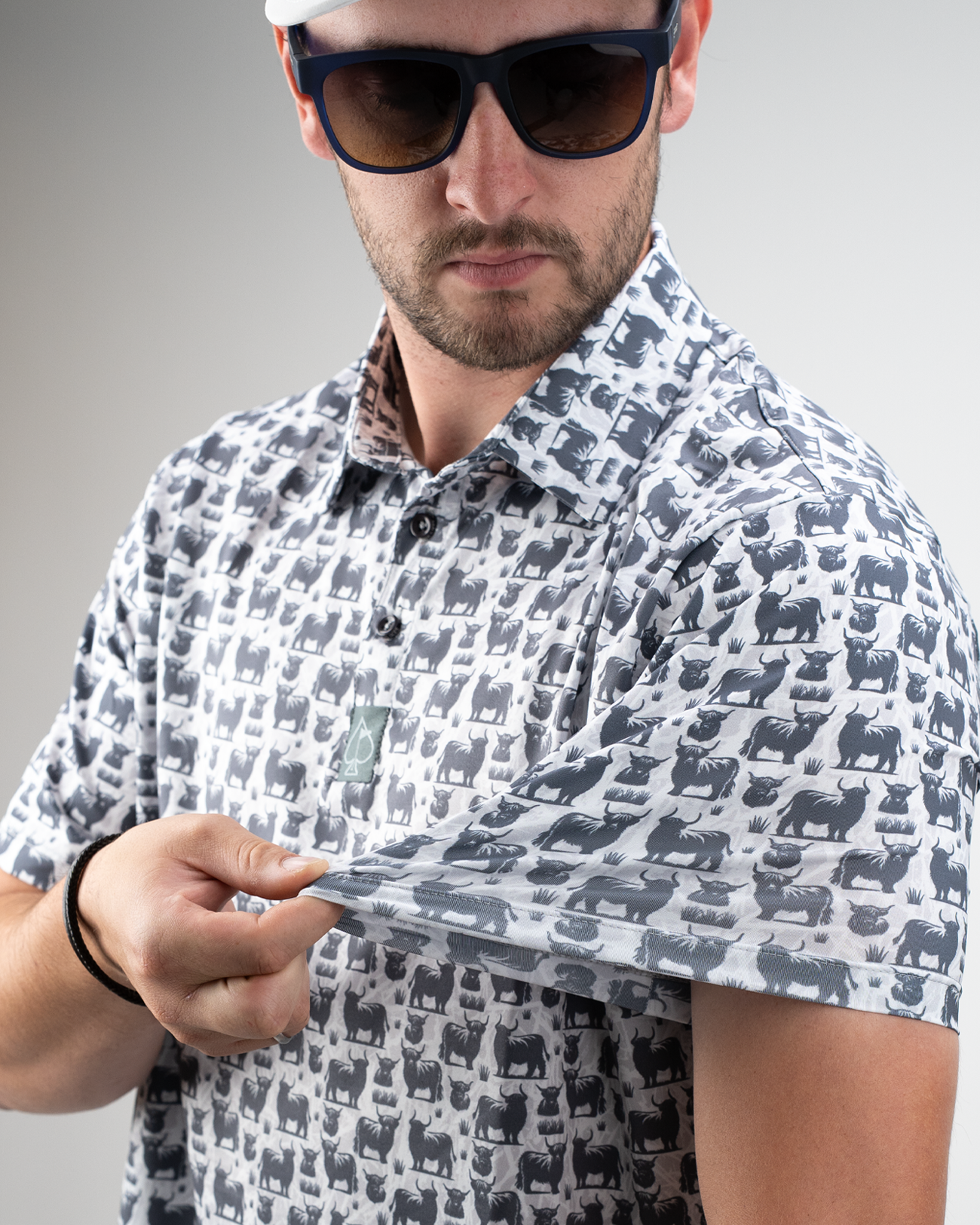 A golfer showcases a Highland Cow patterned shirt, wearing sunglasses and adjusting the sleeve, highlighting its unique design.