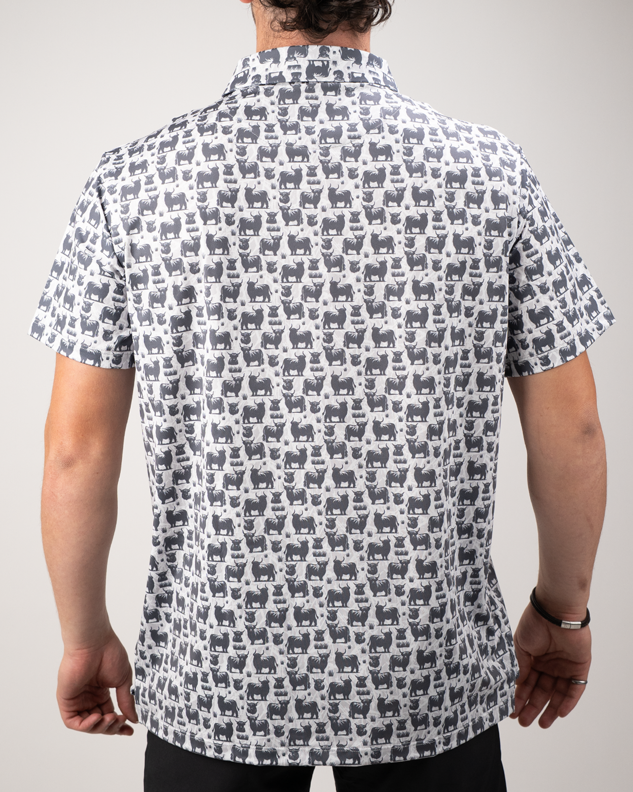 Men's short-sleeve golf shirt featuring a playful Highland cow pattern in gray and blue on a white background.