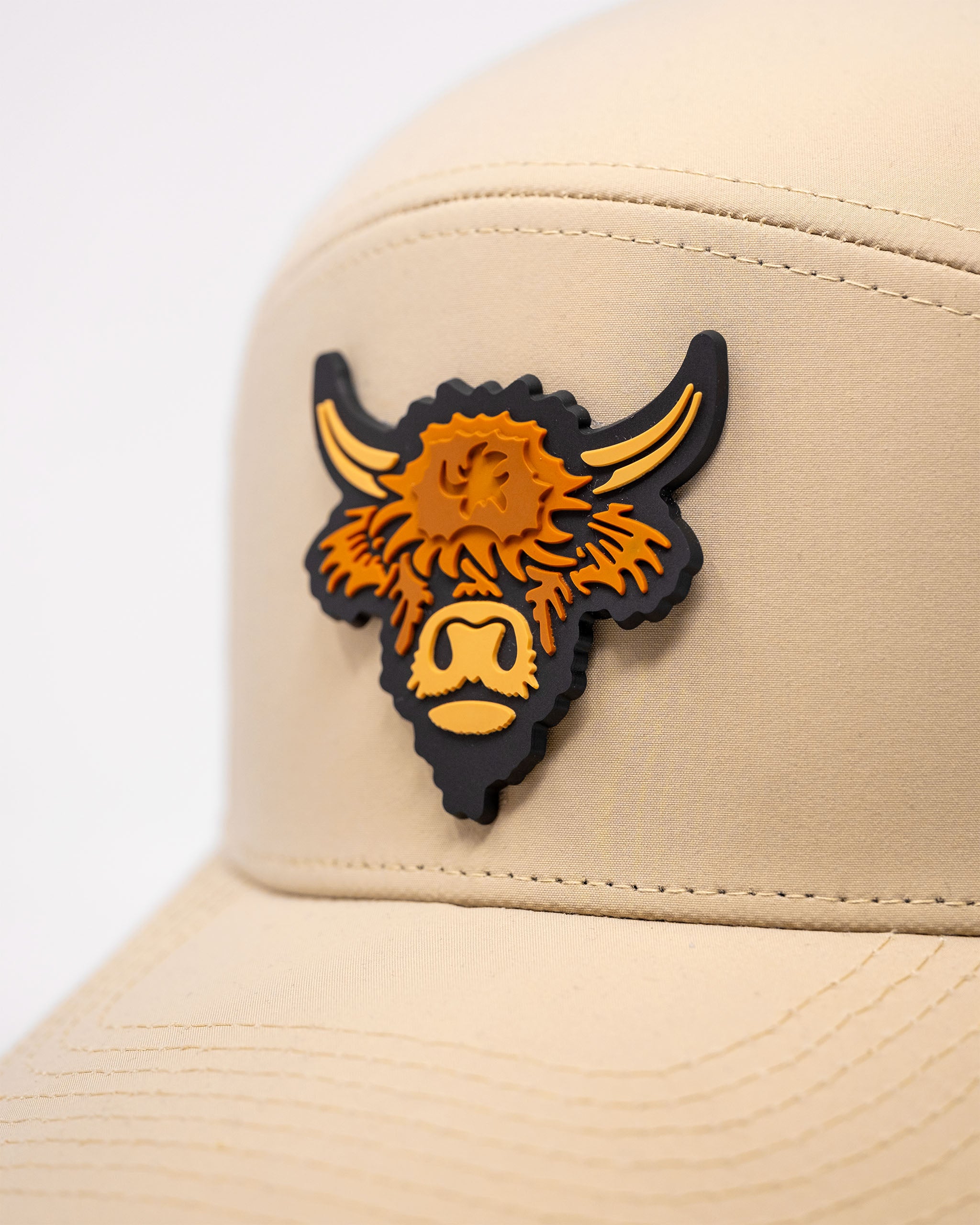 Sand-colored tradesman hat with a Highland cow patch featuring black, orange, and yellow details.