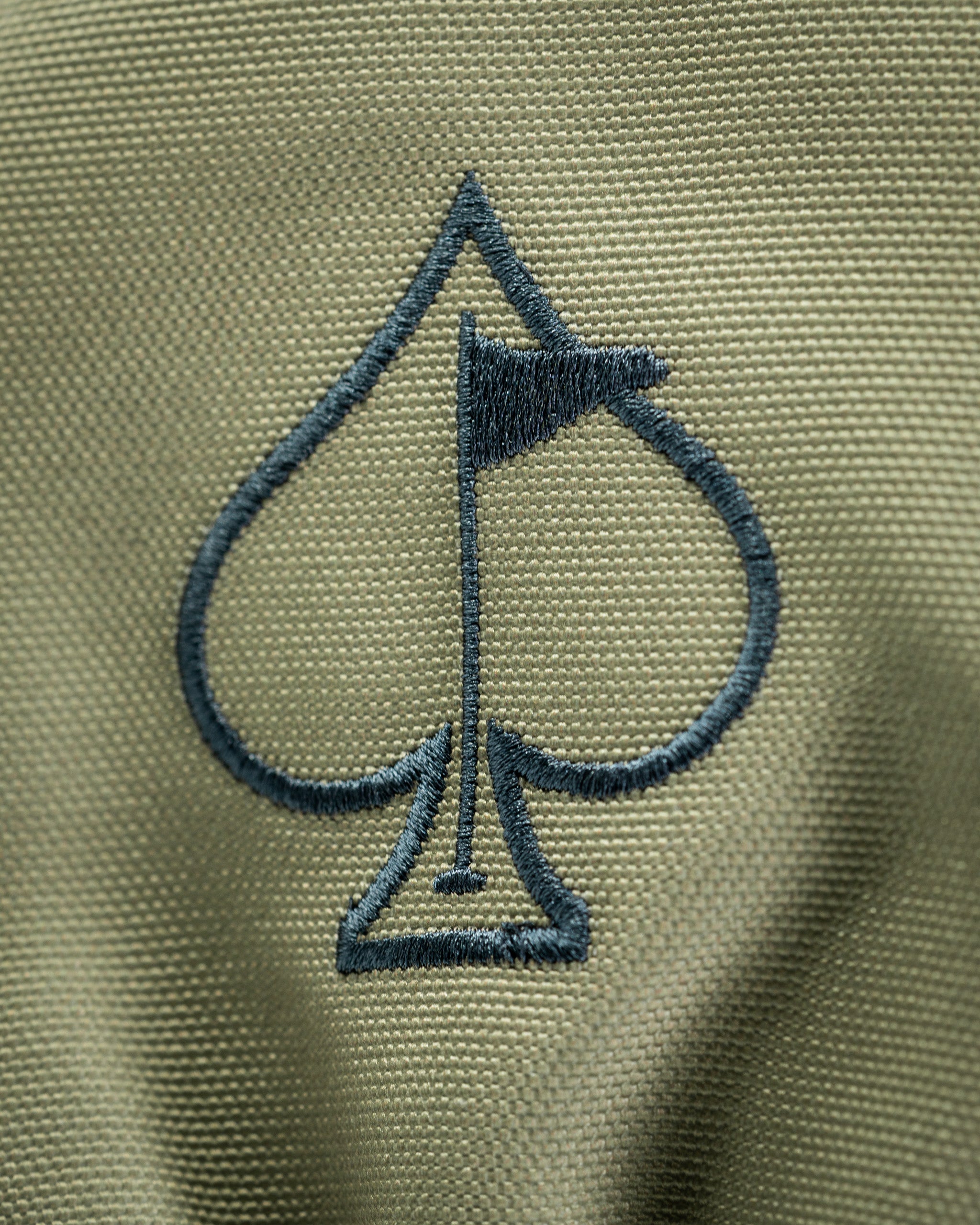 Close-up of a green driver cover featuring a navy blue spade logo with a golf flag, designed for bold golfers.