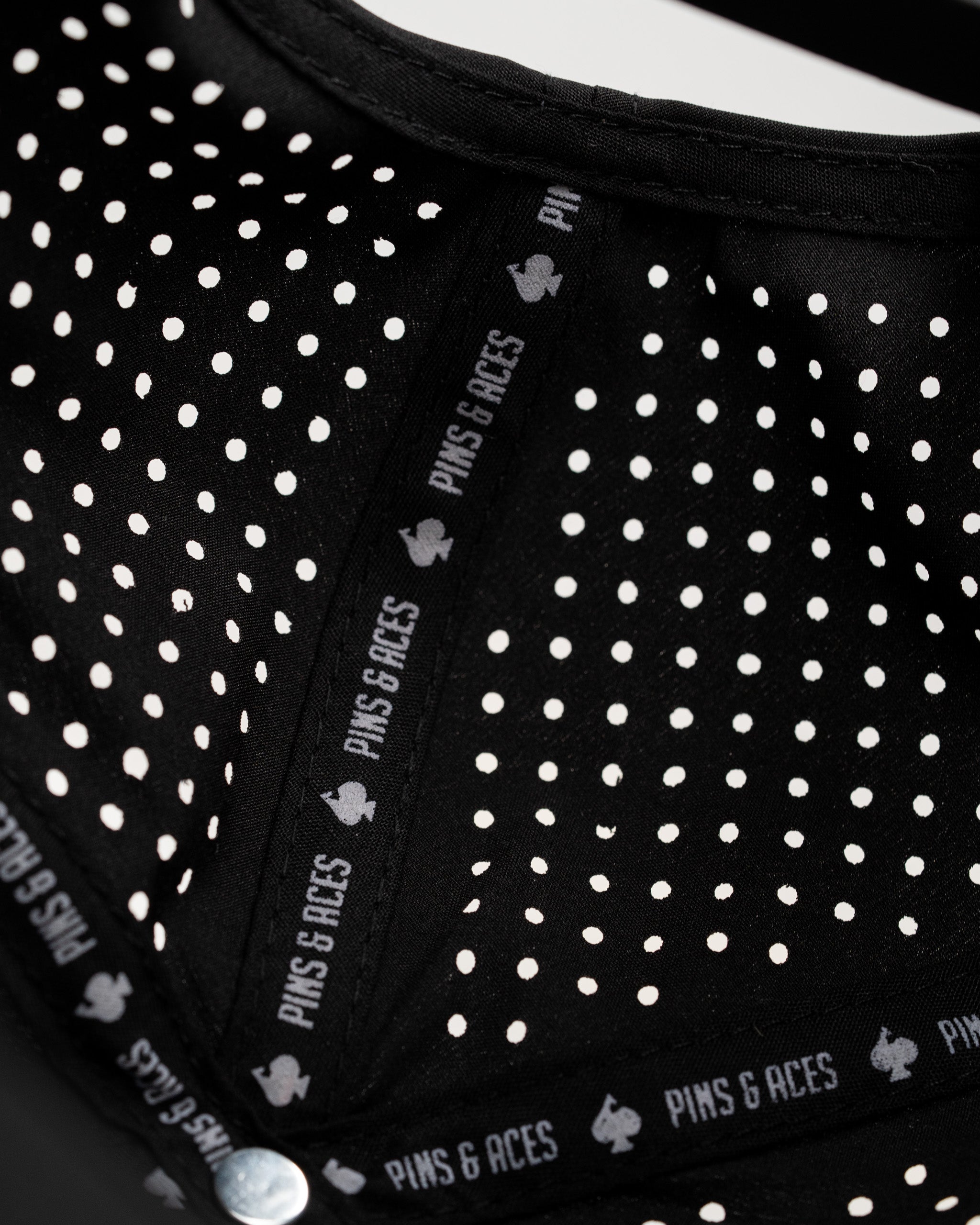 Perforated black rope hat featuring a stylish design and Pins & Aces branding on the interior. Ideal for golfers.