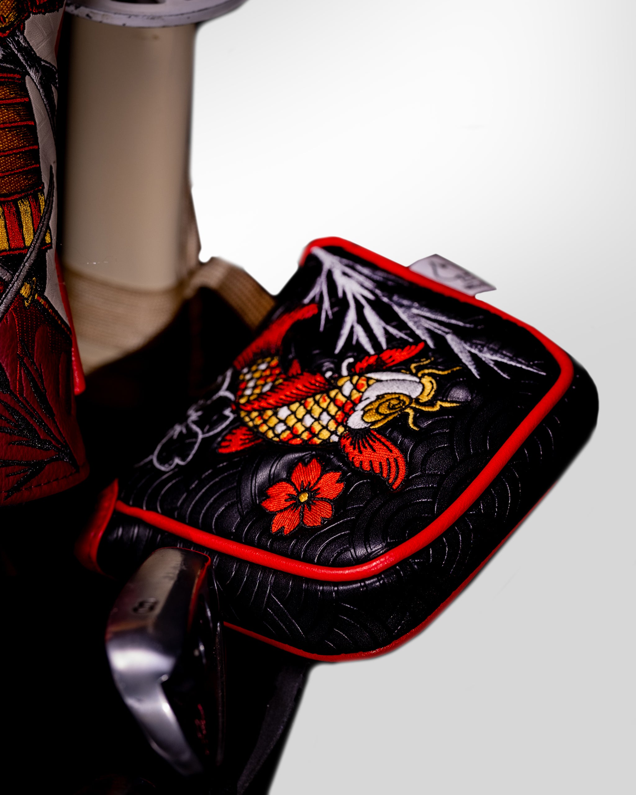 Colorful embroidered koi fish golf headcover with red floral accents on black background, designed to stand out on the cou...