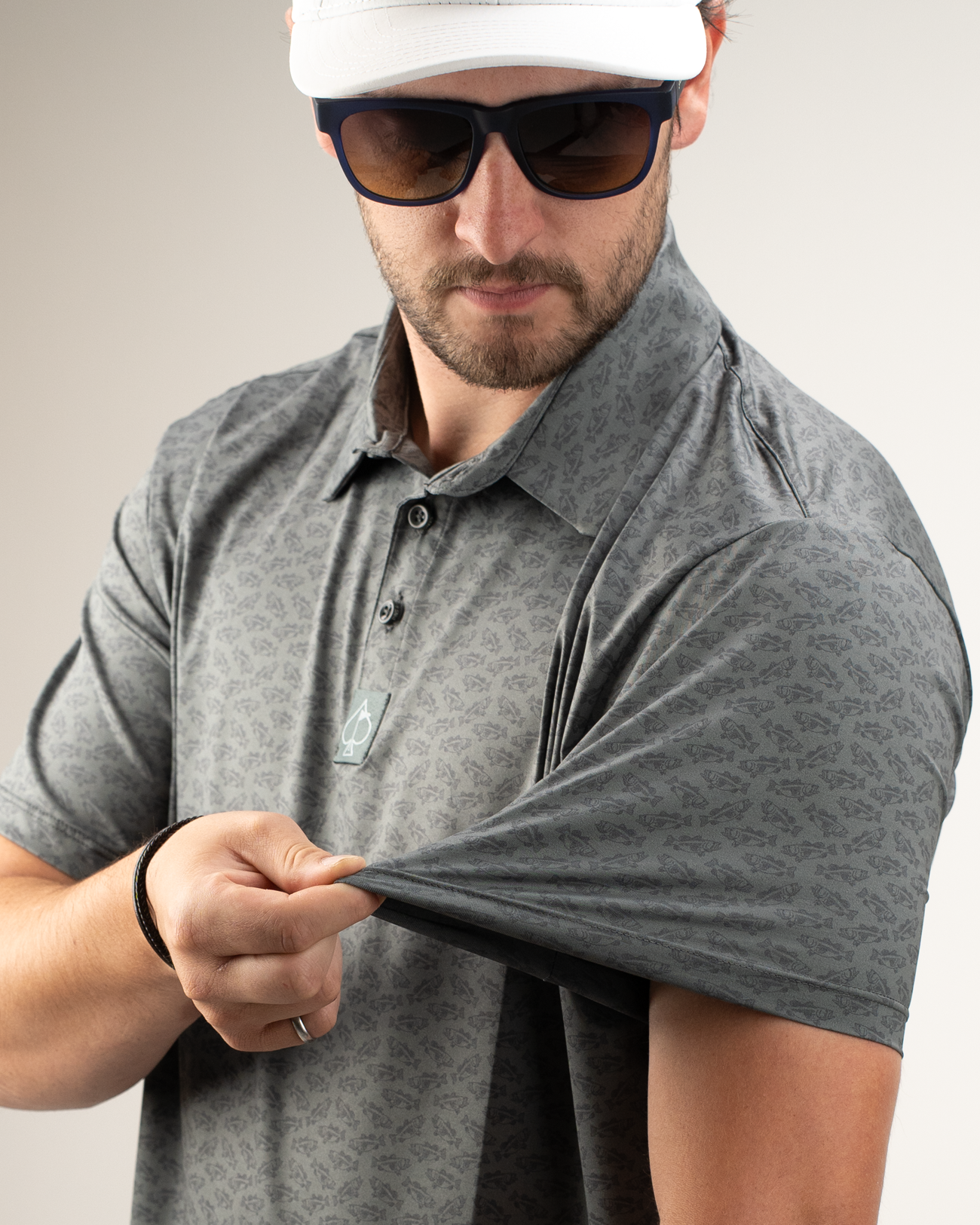 Man showcasing the sleeve of a Large Mouth golf polo shirt with a subtle pattern, wearing sunglasses and a cap.