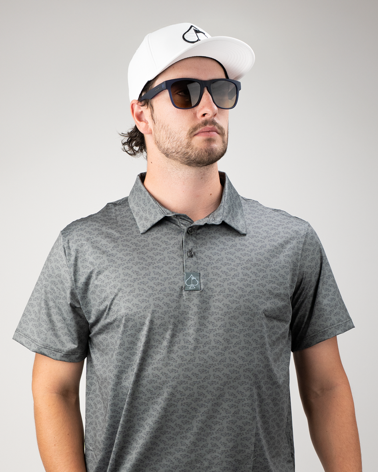 Man wearing a stylish gray golf polo with a subtle pattern, a white cap, and sunglasses, showcasing a modern golf look.