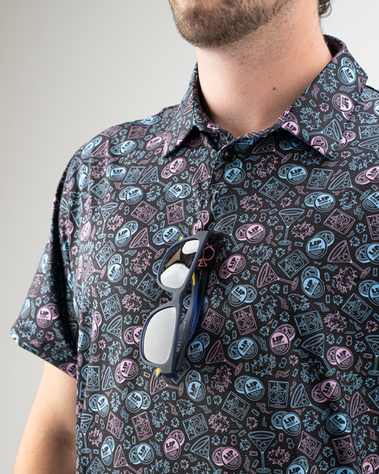 Model wearing a patterned shirt with colorful lip pillow designs, sunglasses resting on the collar.