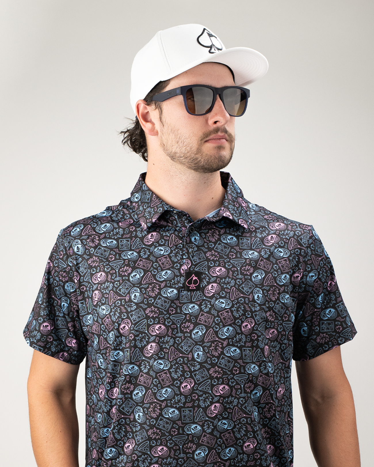 Man wearing a patterned golf shirt featuring colorful lip designs, paired with sunglasses and a white cap.