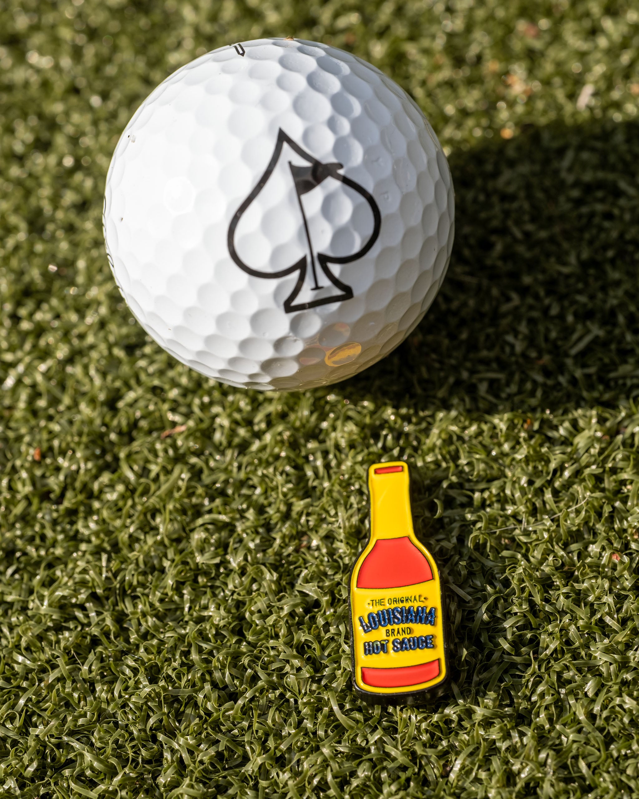 Louisiana Hot Sauce ball marker featuring a vibrant red color and iconic branding, displayed alongside a golf ball.