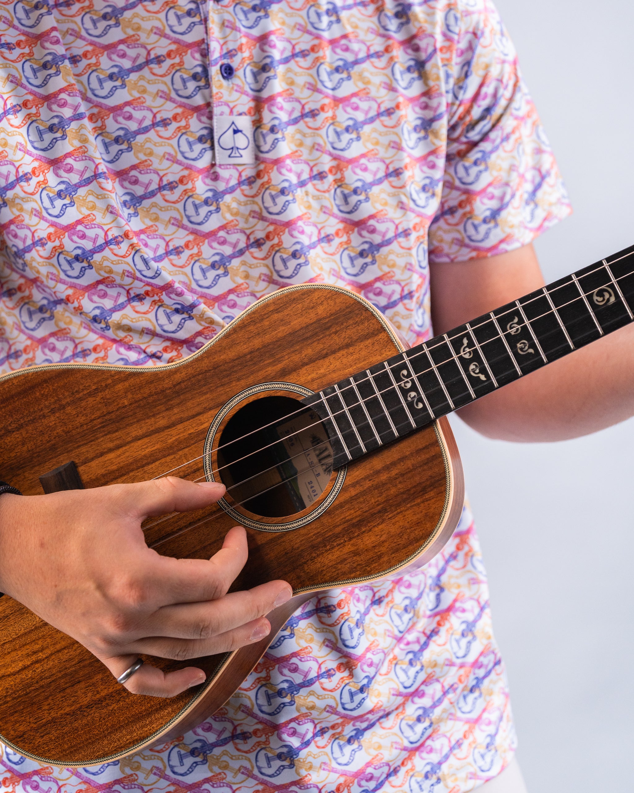 Person in colorful guitar-themed shirt holding a wooden ukulele, highlighting bold, playful golf apparel and accessories.