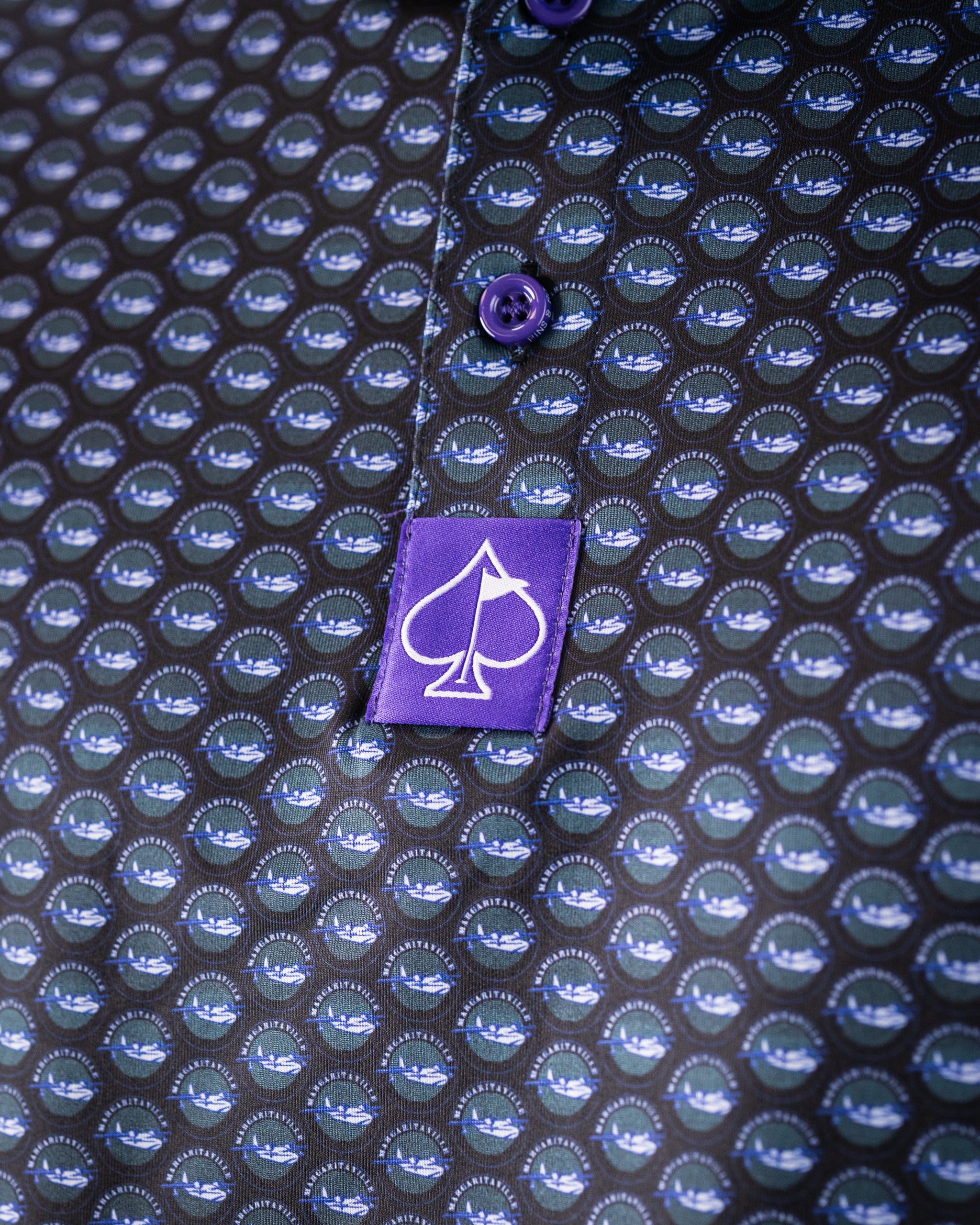 Close-up of a golf shirt with a bold, repeating logo pattern in blue and green on black, purple buttons, and a purple logo...