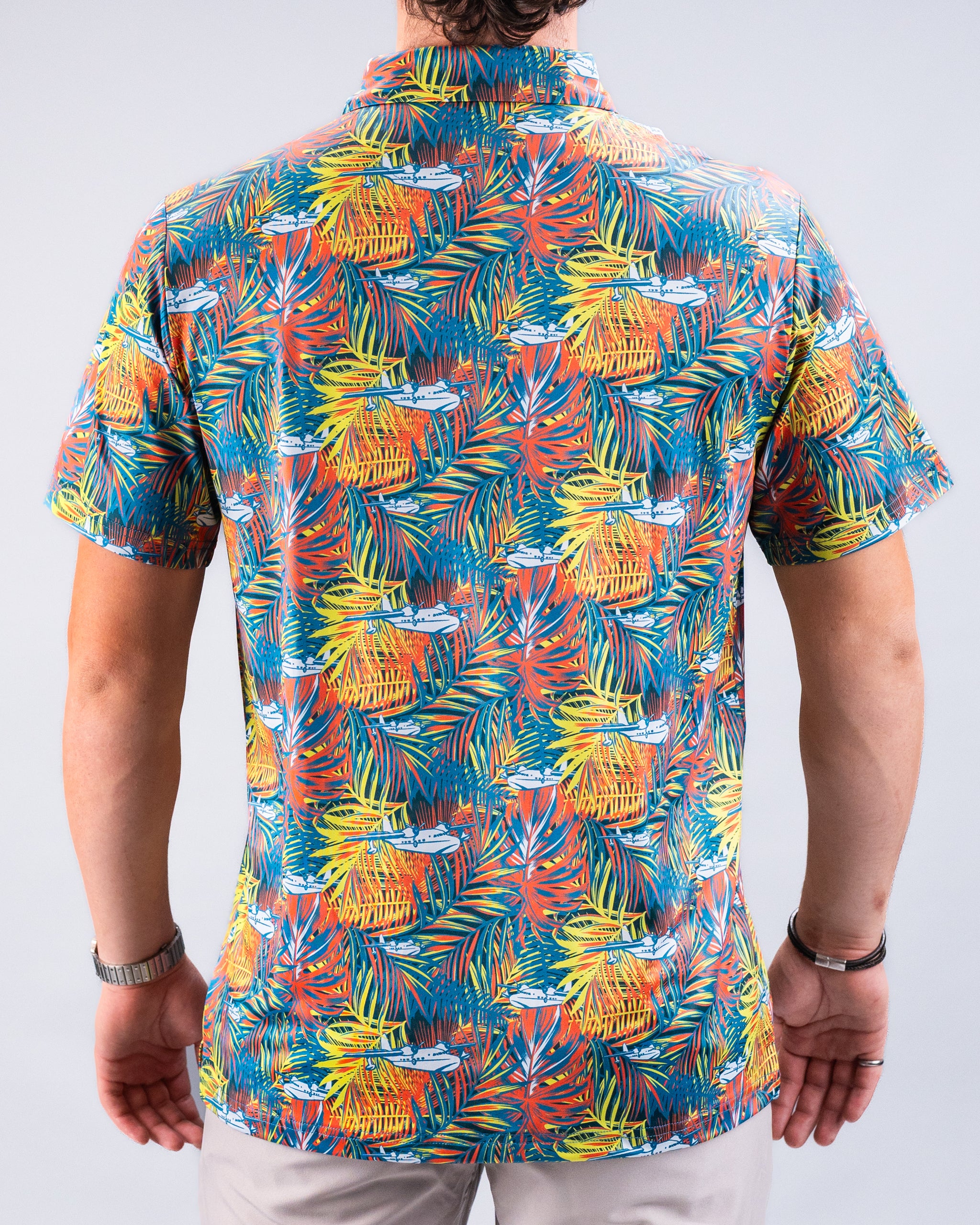 Bright tropical print golf shirt with palm leaves, colorful foliage, and small white airplanes. Perfect for bold golf style.