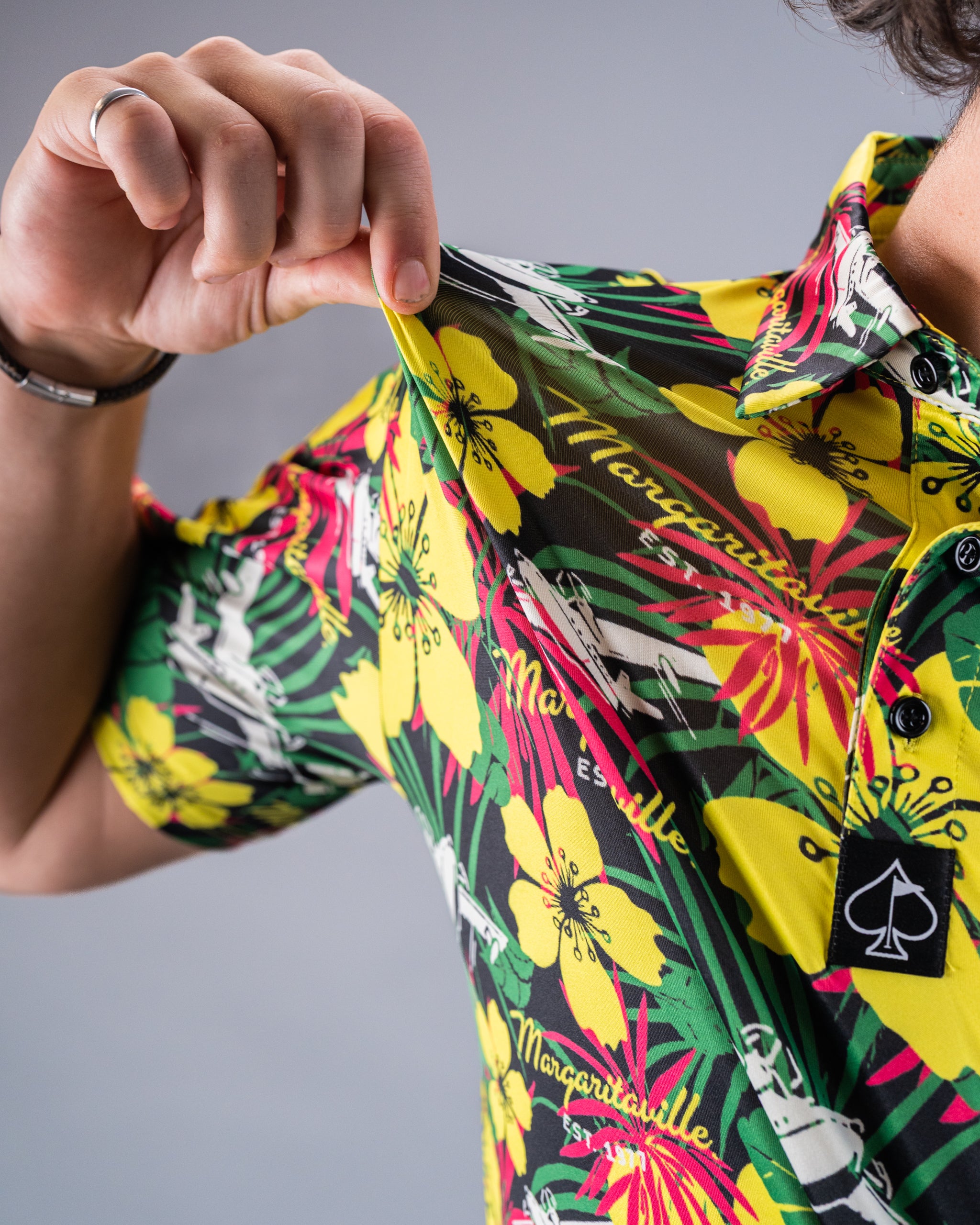 Close-up of a person wearing a vibrant, tropical floral golf shirt with yellow, pink, green, and black colors, emphasizing...