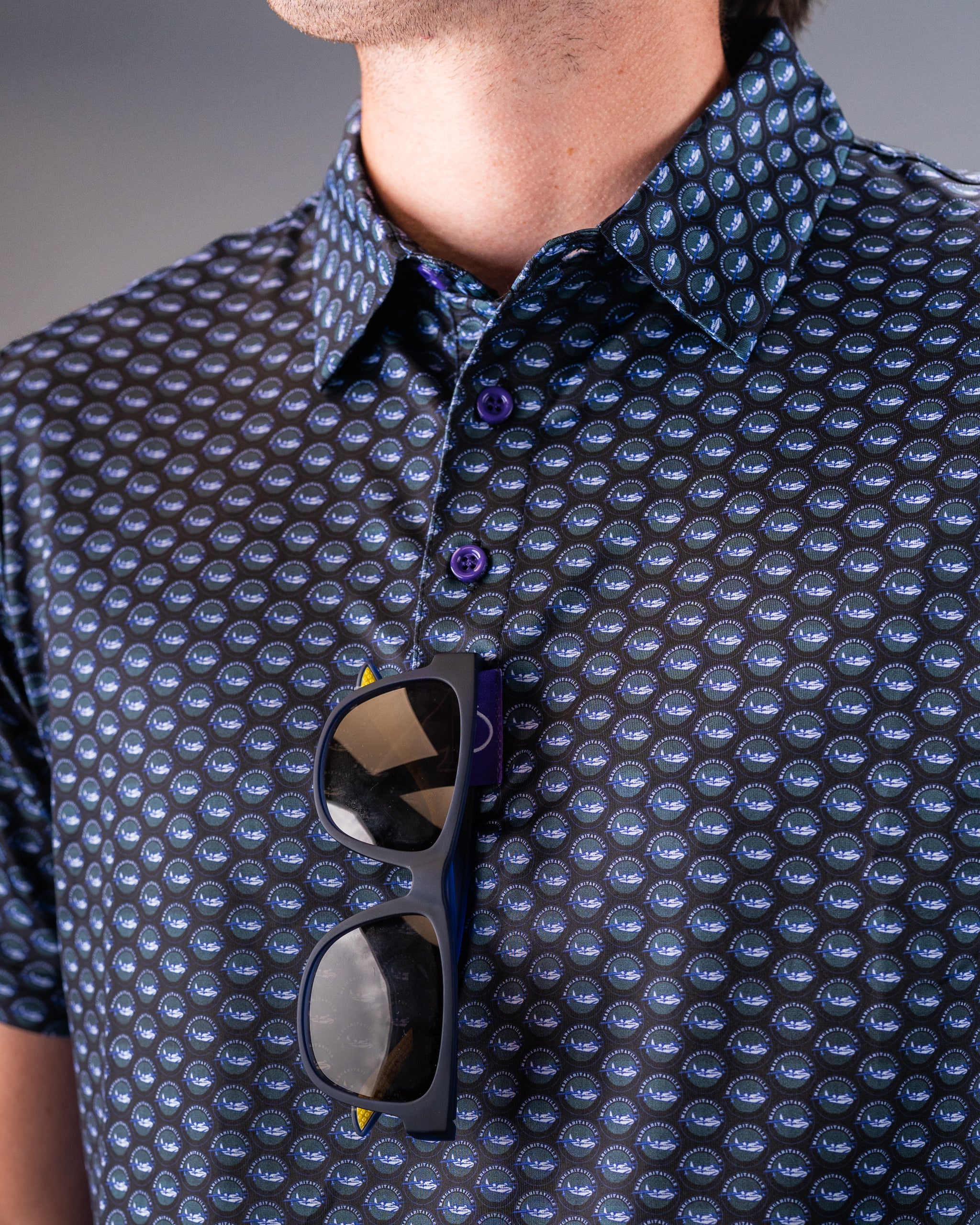 Close-up of a golfer's shirt with a bold, repeating pattern of golf balls, featuring blue and purple tones, with sunglasse...
