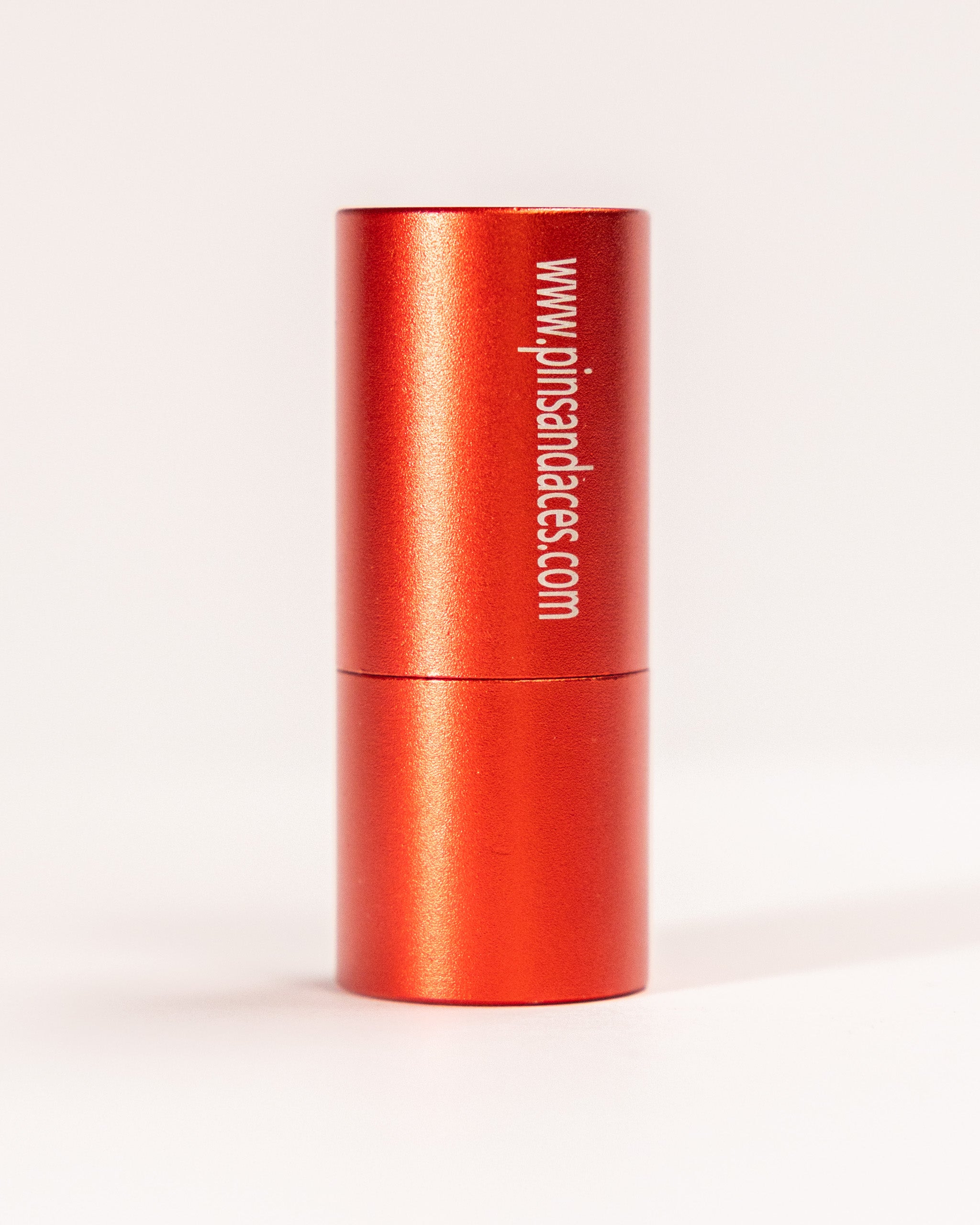 Red cylindrical container with white text displaying a website URL, containing a middle finger ball stamp for novelty use.