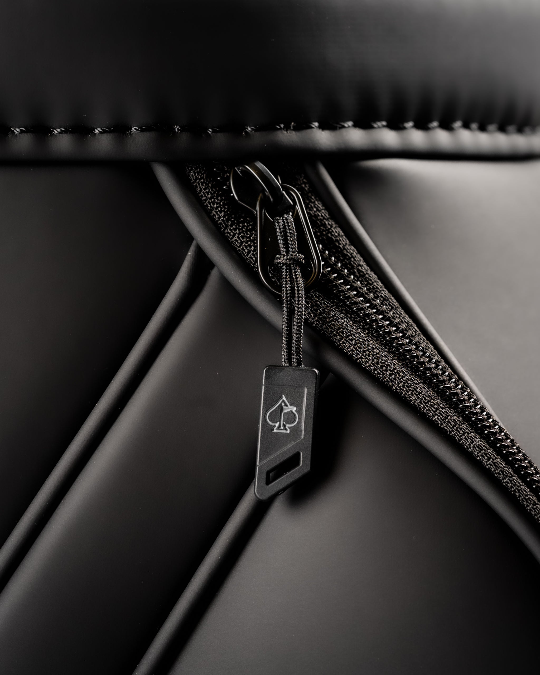 Close-up of the Den Caddy in Obsidian, featuring a sleek black zipper and stylish spade logo pull tab.