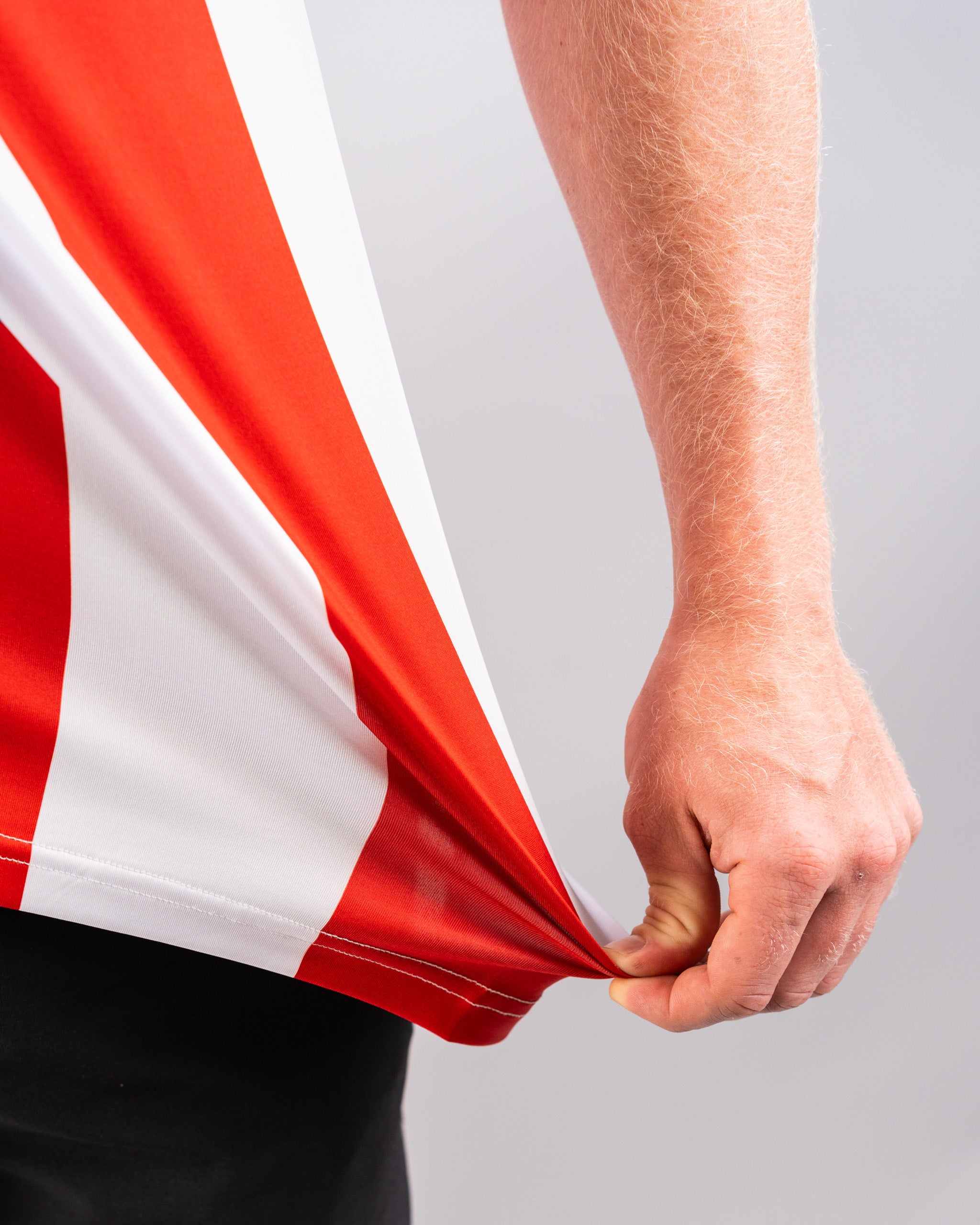 Close-up of a person holding the corner of a red and white American flag, with visible arm and hand against a plain background.