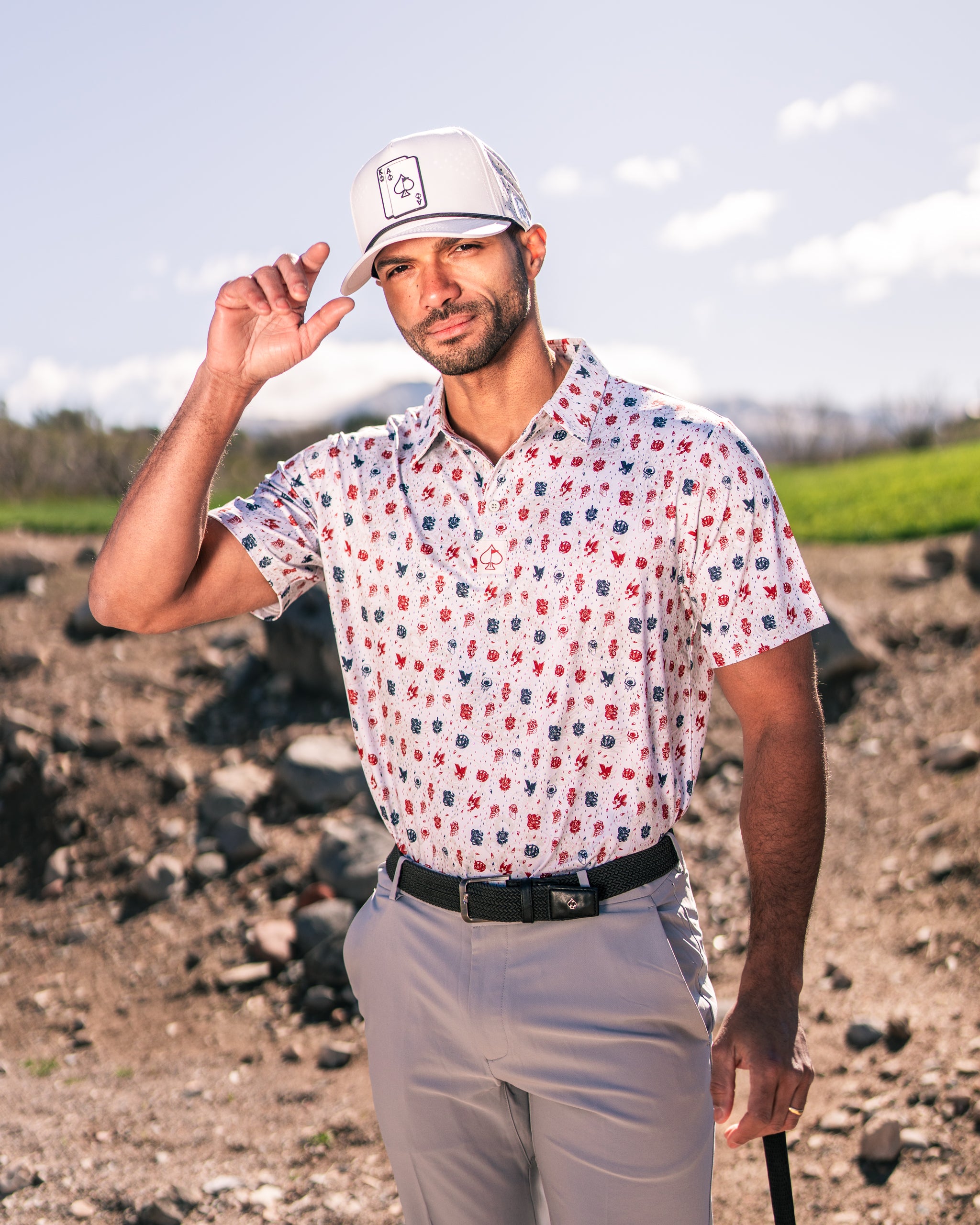 Man wearing a colorful American Traditional golf polo shirt and a white cap, posing outdoors on a golf course.