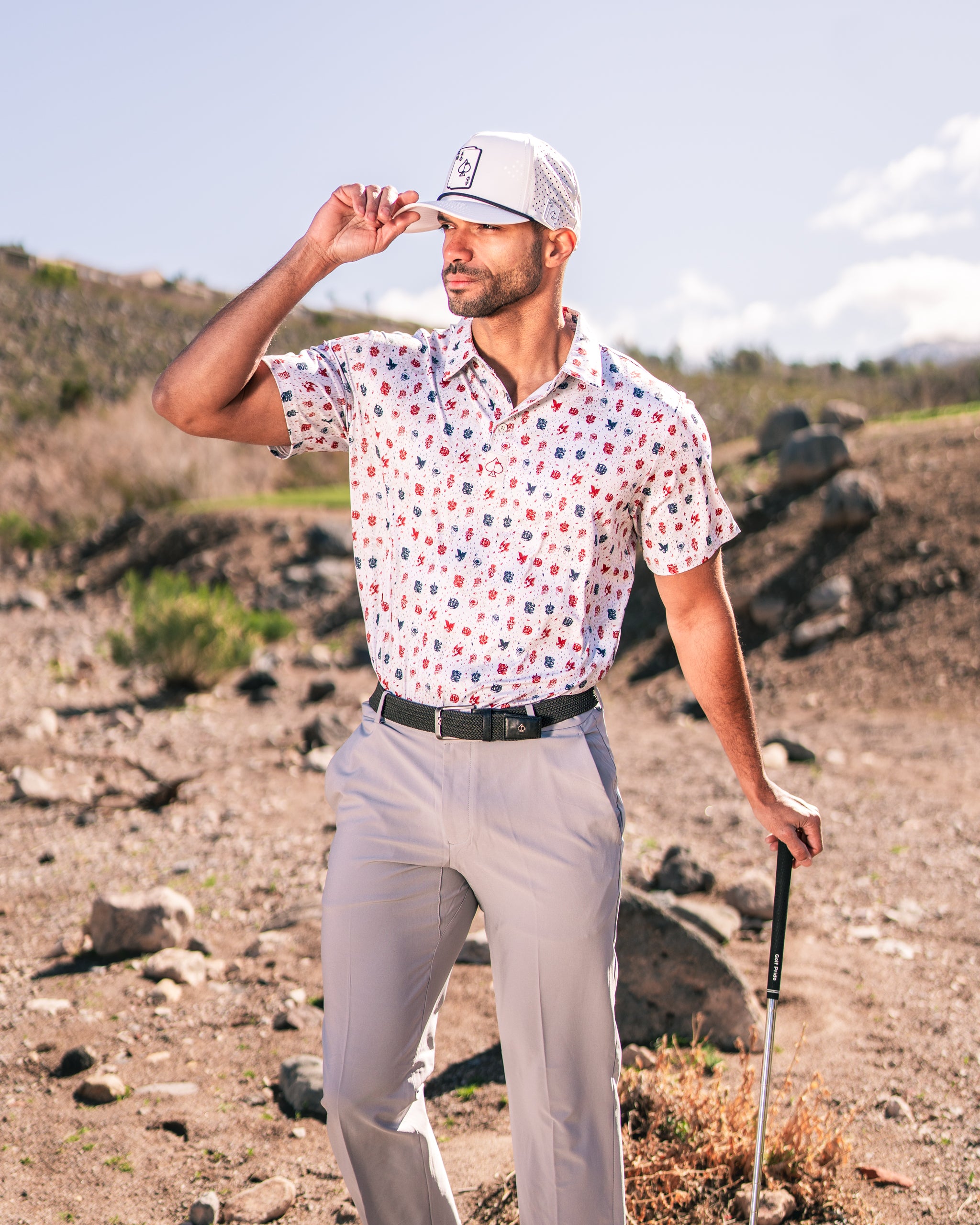 A golfer poses confidently in an American Traditional polo shirt with a floral pattern, paired with light trousers and a cap.