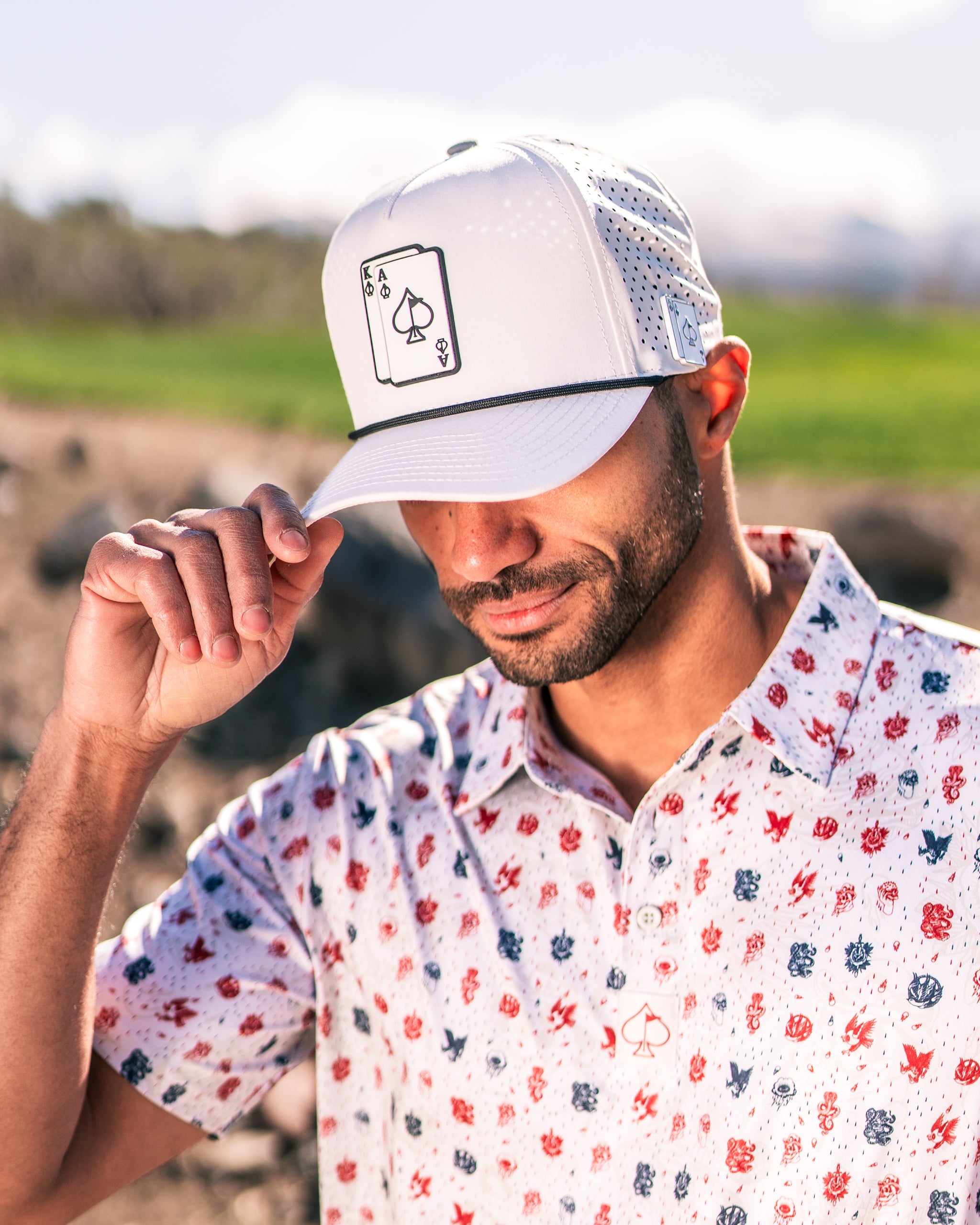 Stylish golfer wearing a white cap with an ace of spades design, paired with a colorful patterned shirt on a sunny day.