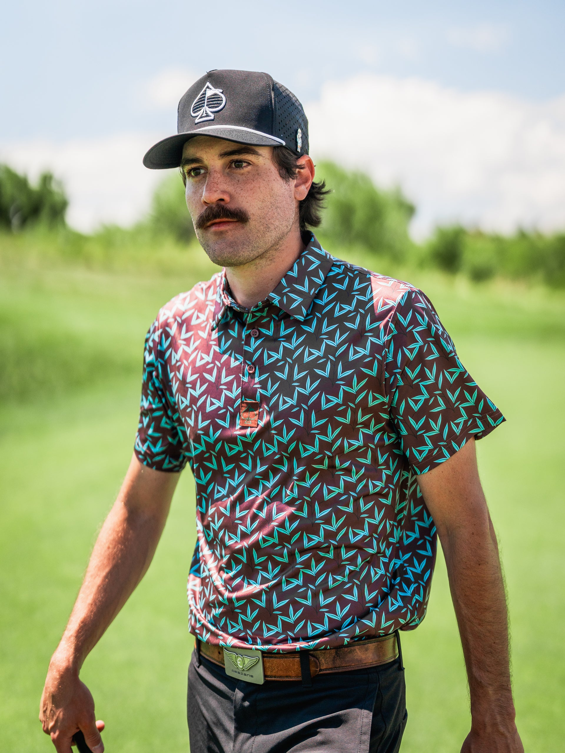 Bold golf shirt with a colorful geometric pattern, worn by a man on a sunny golf course, showcasing a stylish look.